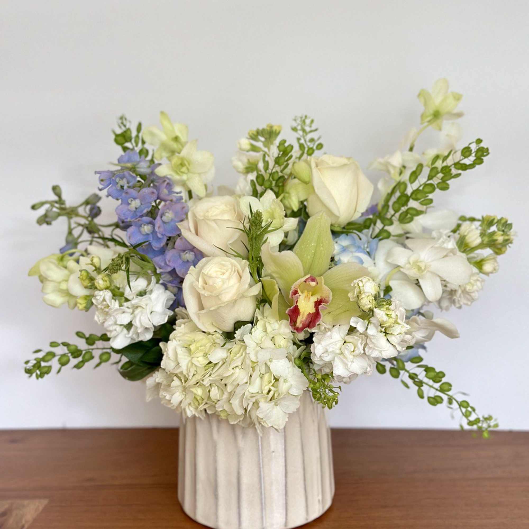 Mixed bouquet in a cream ribbed vase with white, pale pink, and blue flowers