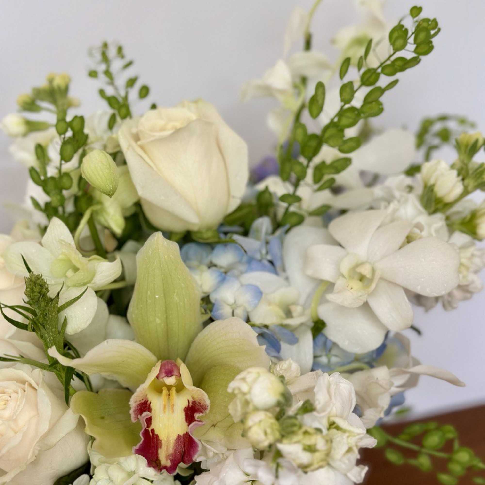 White floral bouquet with orchids, roses, and pale blue accents