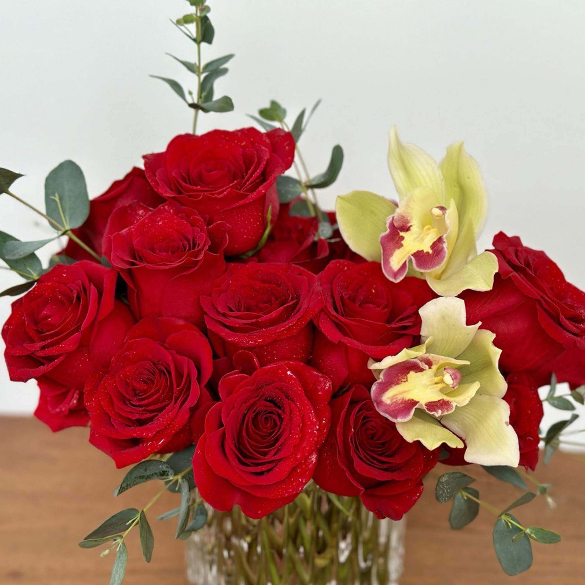 Red roses with pale yellow orchids in a clear glass vase