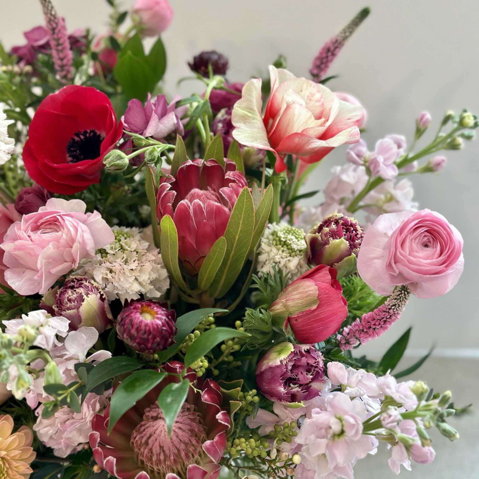 Mixed pink and red bouquet with protea and ranunculus in a glass vase