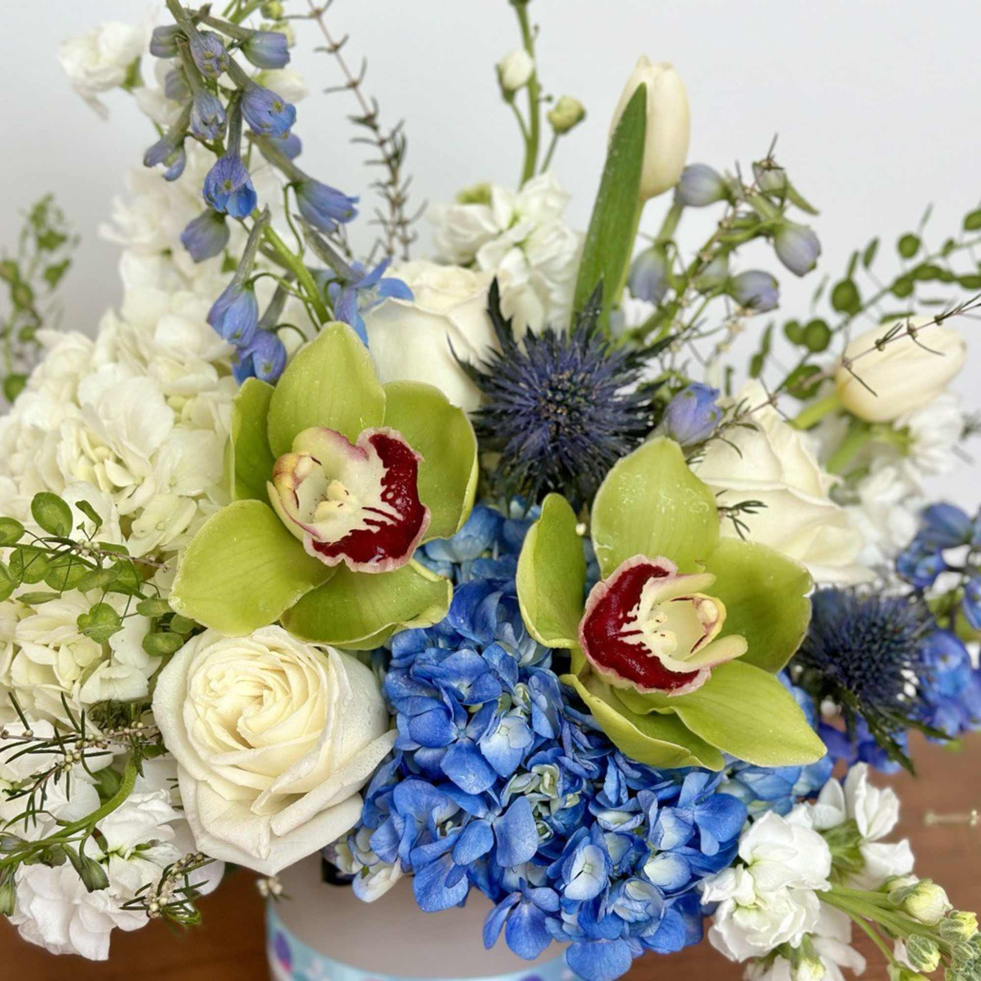 Blue and white floral arrangement with green orchids in a vase
