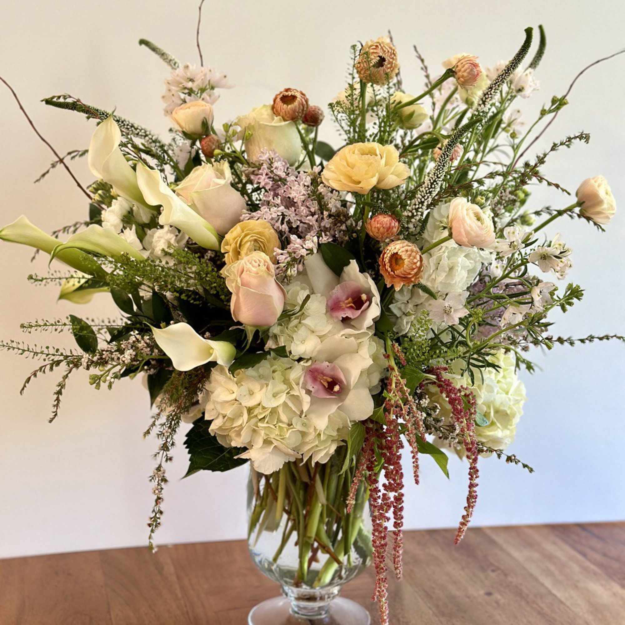 Tall arrangement of white hydrangeas, calla lilies, and pastel roses in a clear glass vase