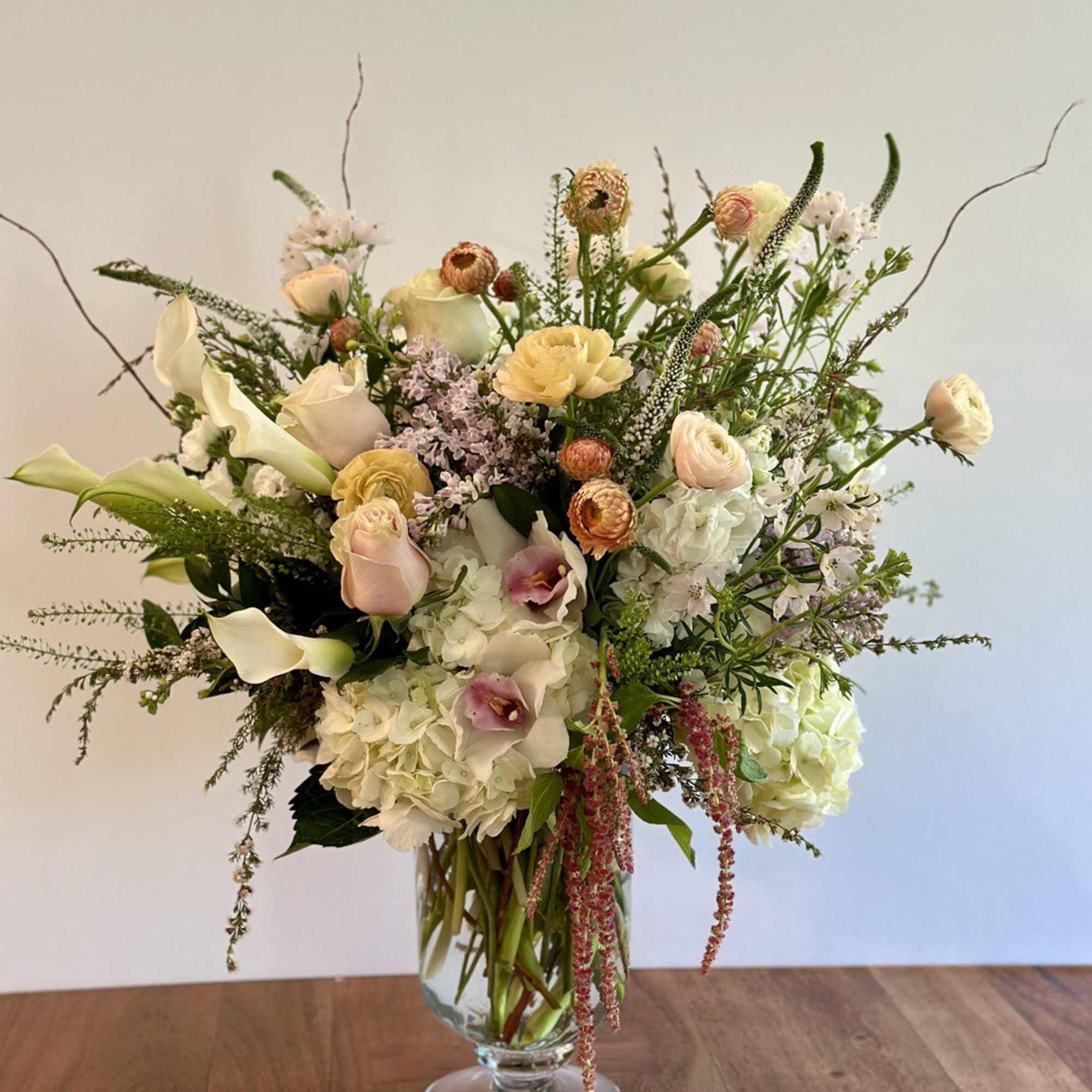 Tall arrangement of white hydrangeas, blush roses, and mixed pastel flowers in a clear glass vase