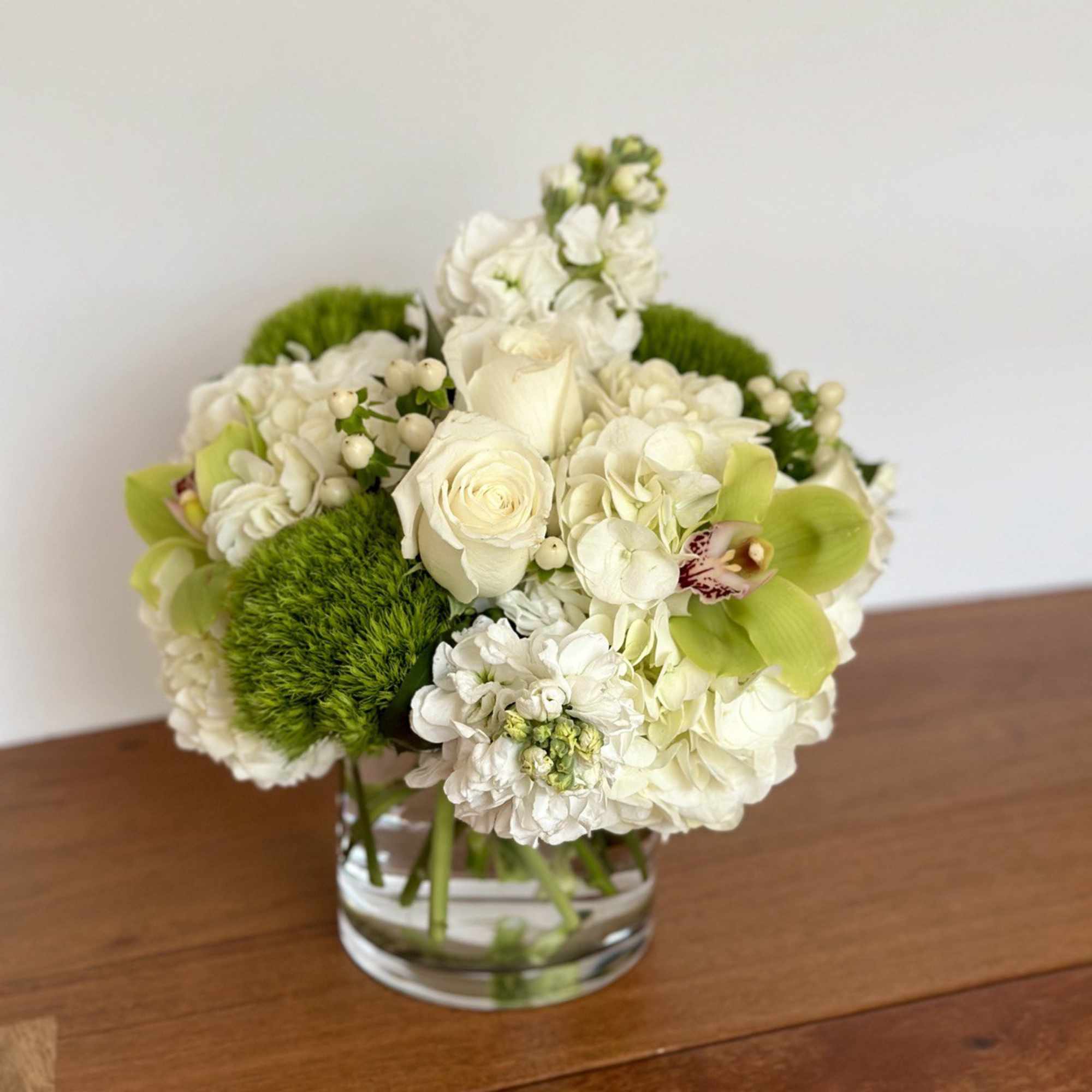 White floral arrangement in a clear glass vase with bright green accents