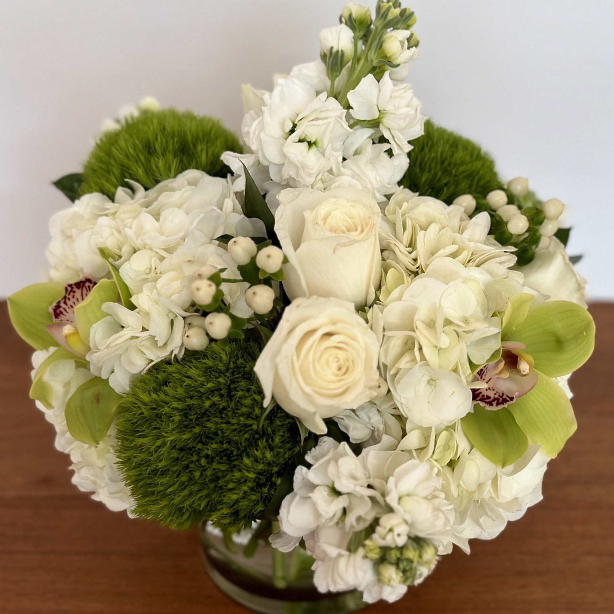 White floral bouquet with green orchids and mossy green accents in a glass vase