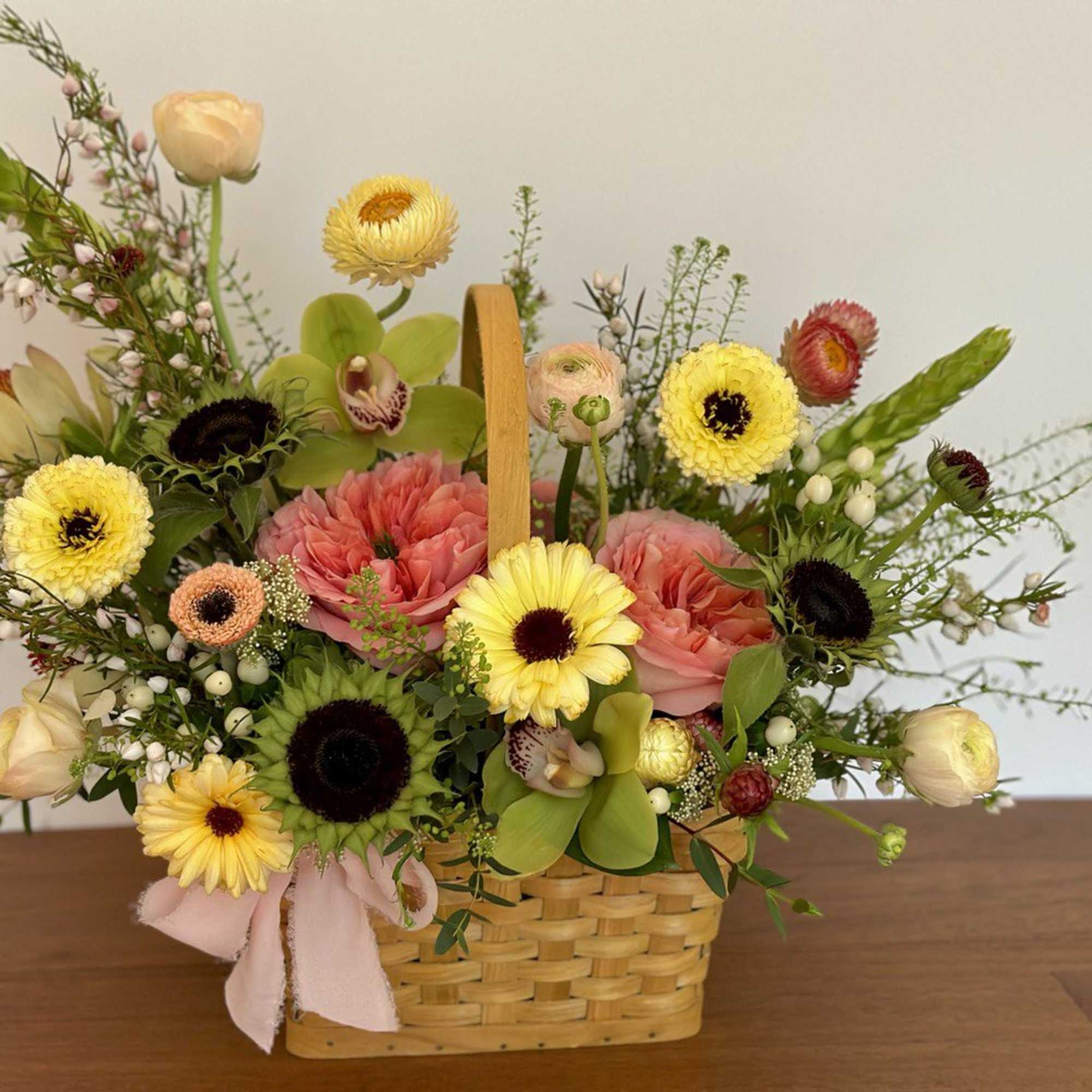 Mixed flower arrangement in a woven basket with a pink ribbon, photo 2 of 4