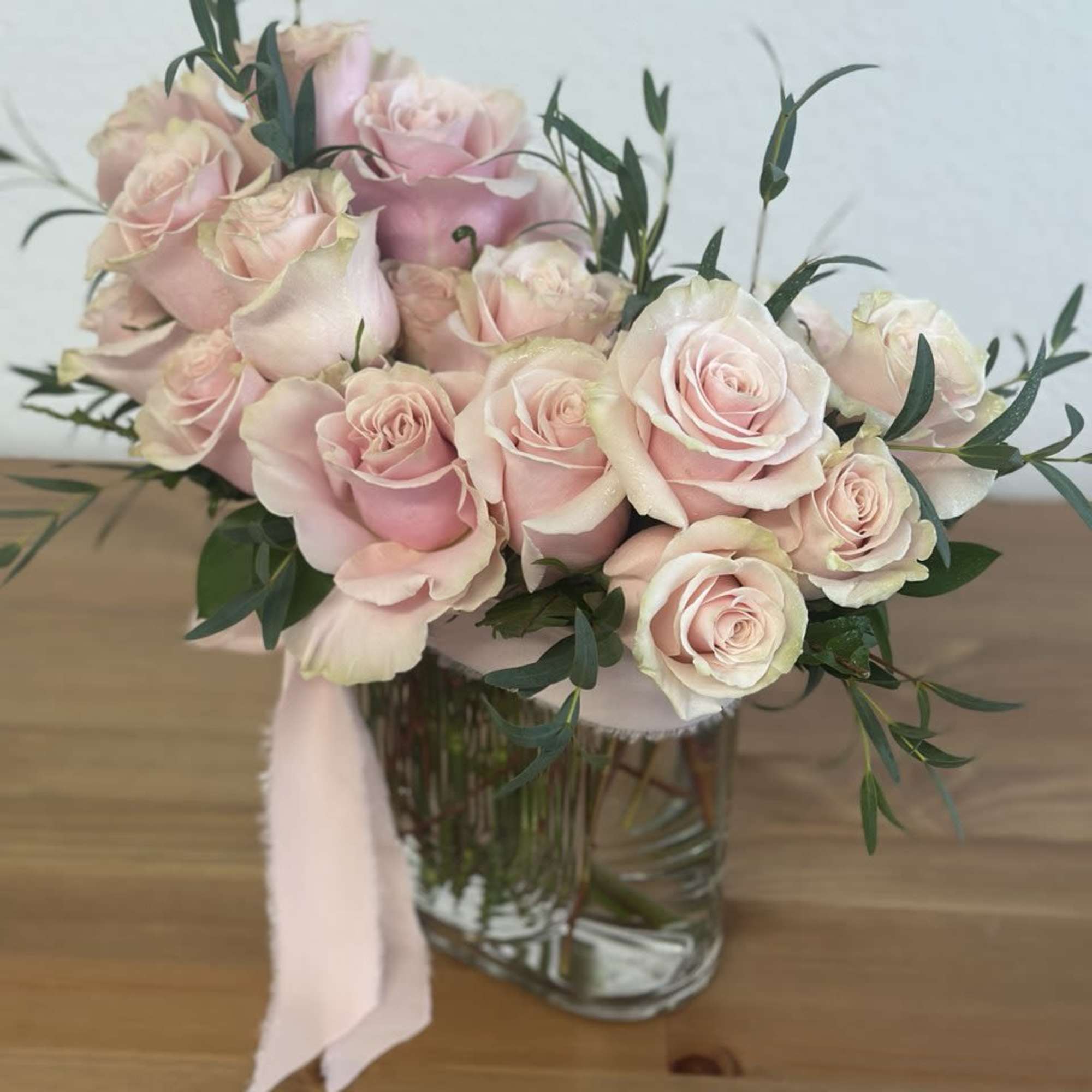 Bouquet of pale pink roses in a clear glass vase with a pink ribbon