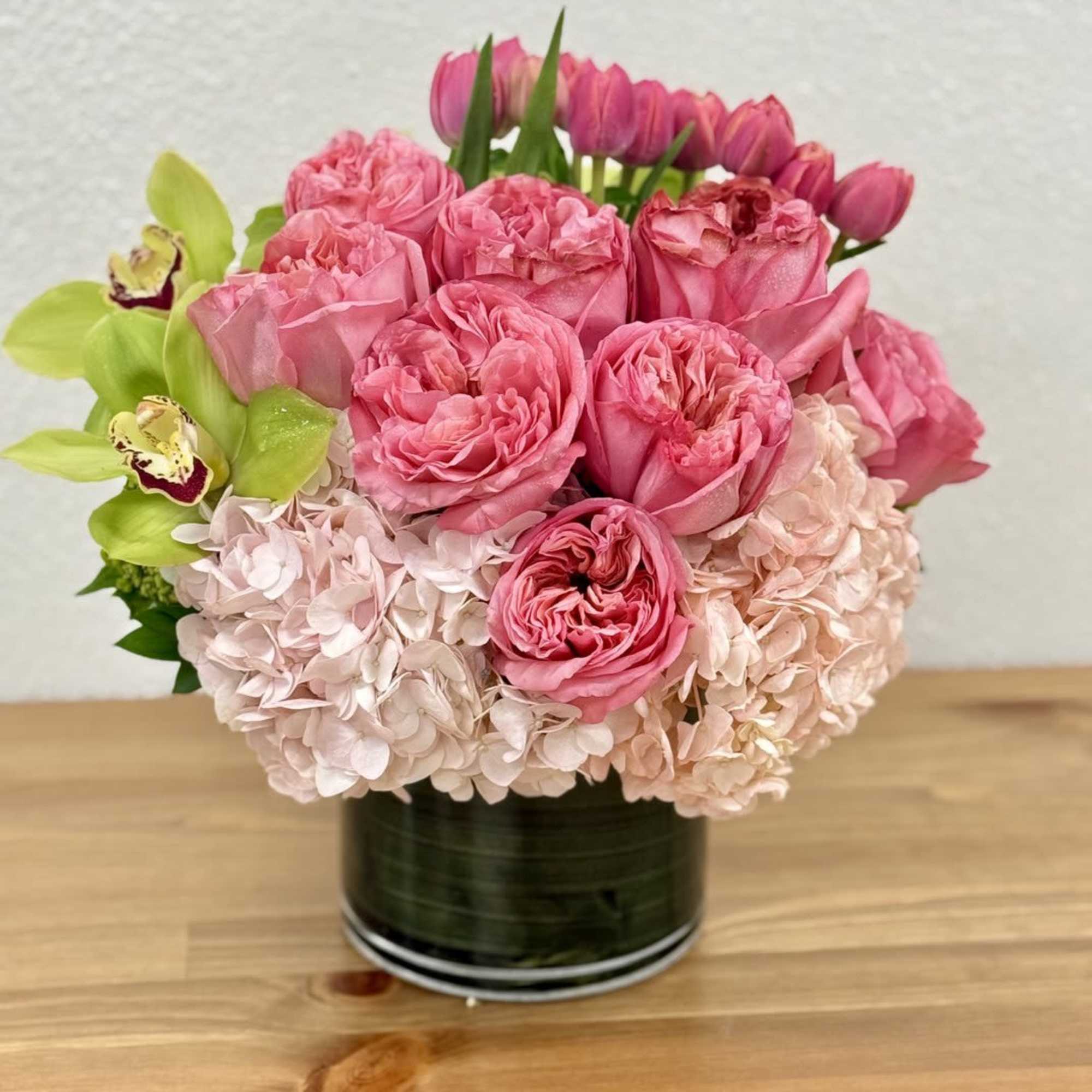 Pink roses and hydrangeas in a black vase with green orchids