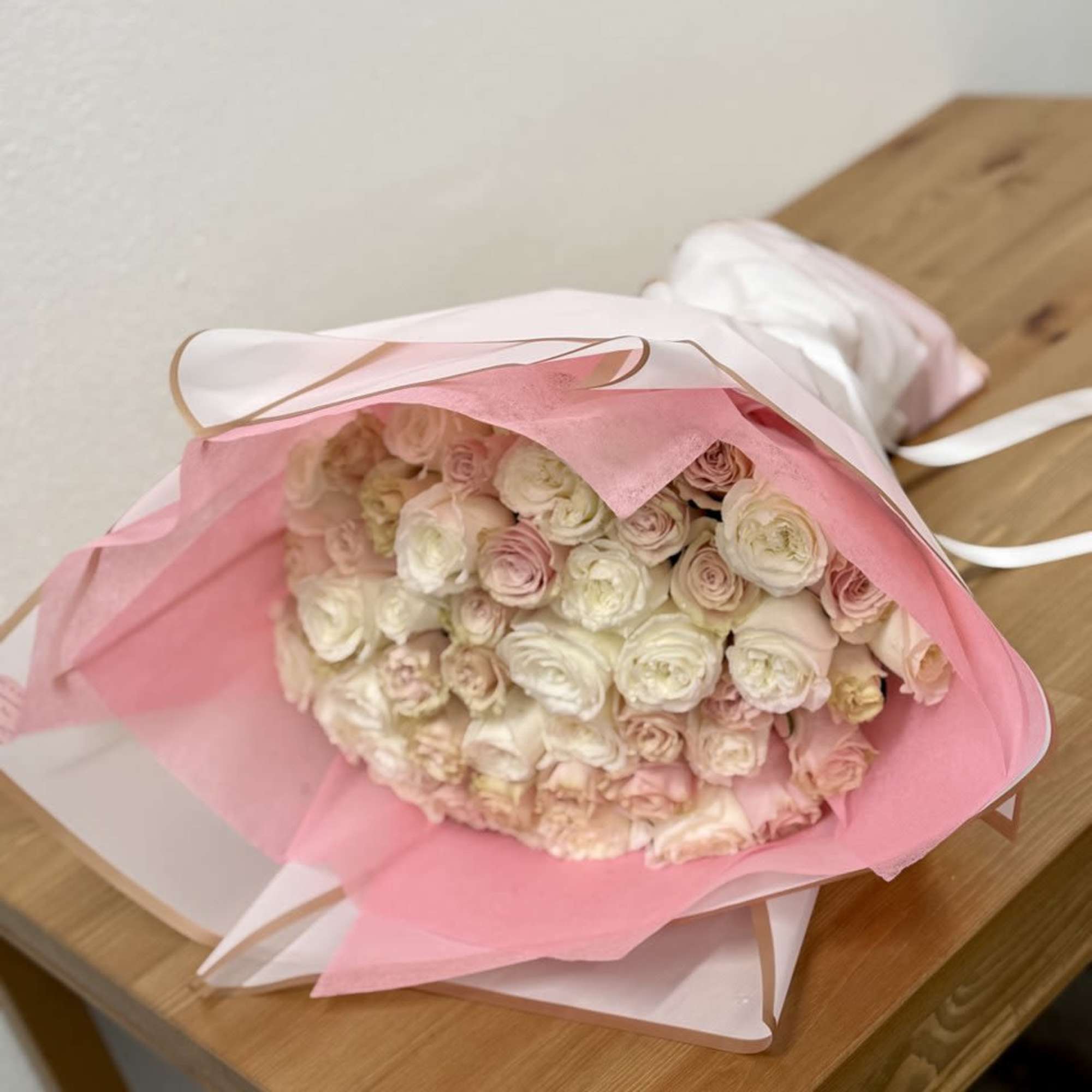 Bouquet of pale pink and white roses wrapped in pink paper