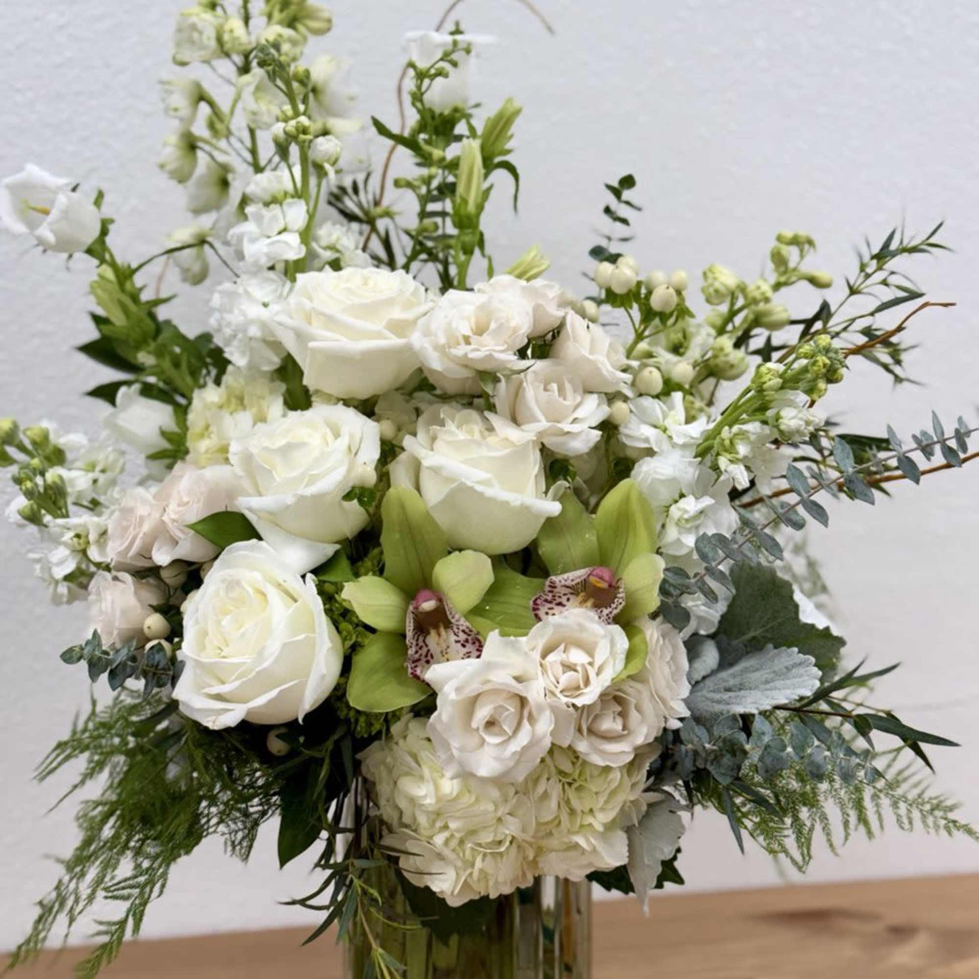 White roses and orchids arranged in a clear glass vase