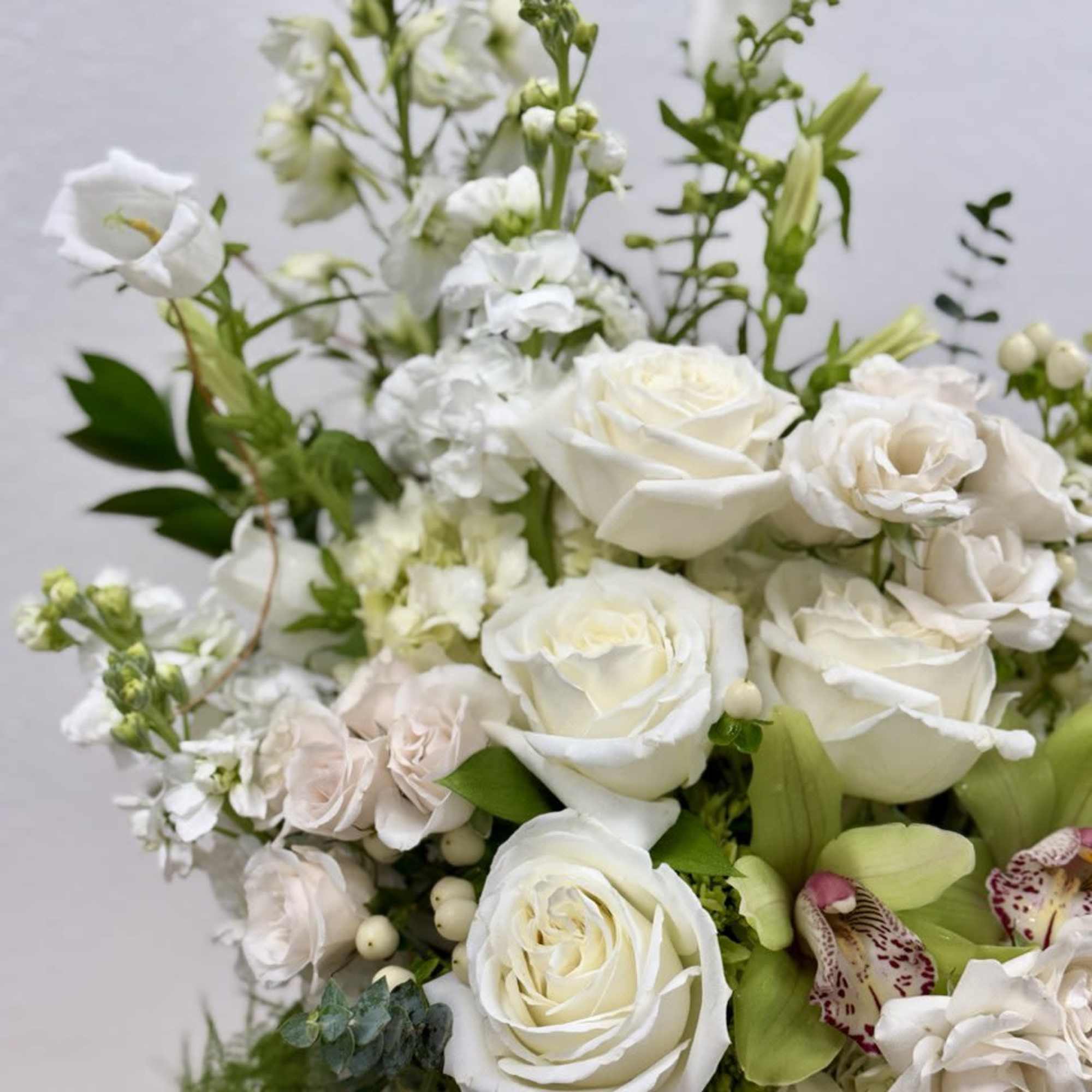 White roses and orchids arranged in a bouquet with green accents