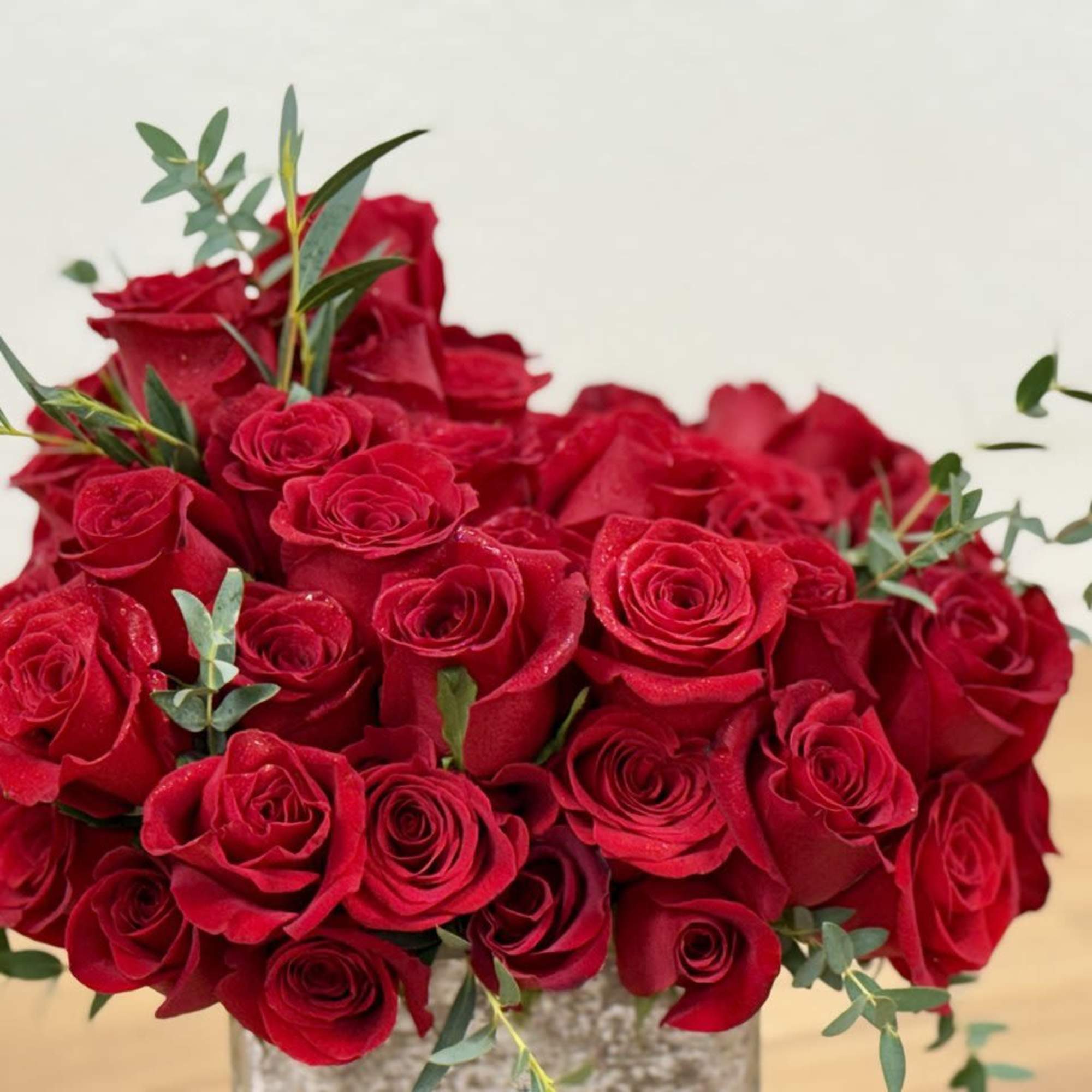 Bouquet of red roses with small eucalyptus sprigs in a clear vase