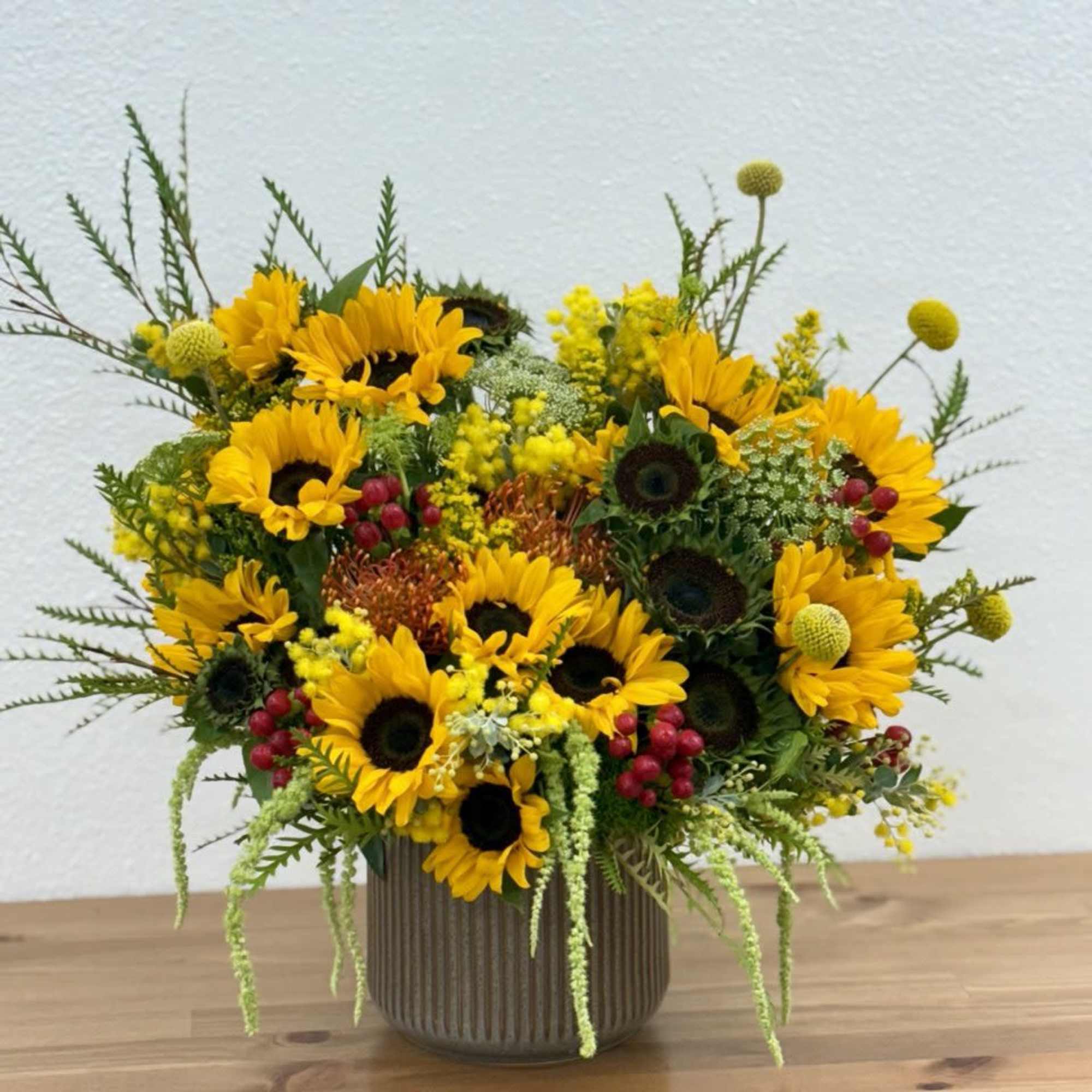 Sunflower arrangement in a ribbed vase with yellow and red accents