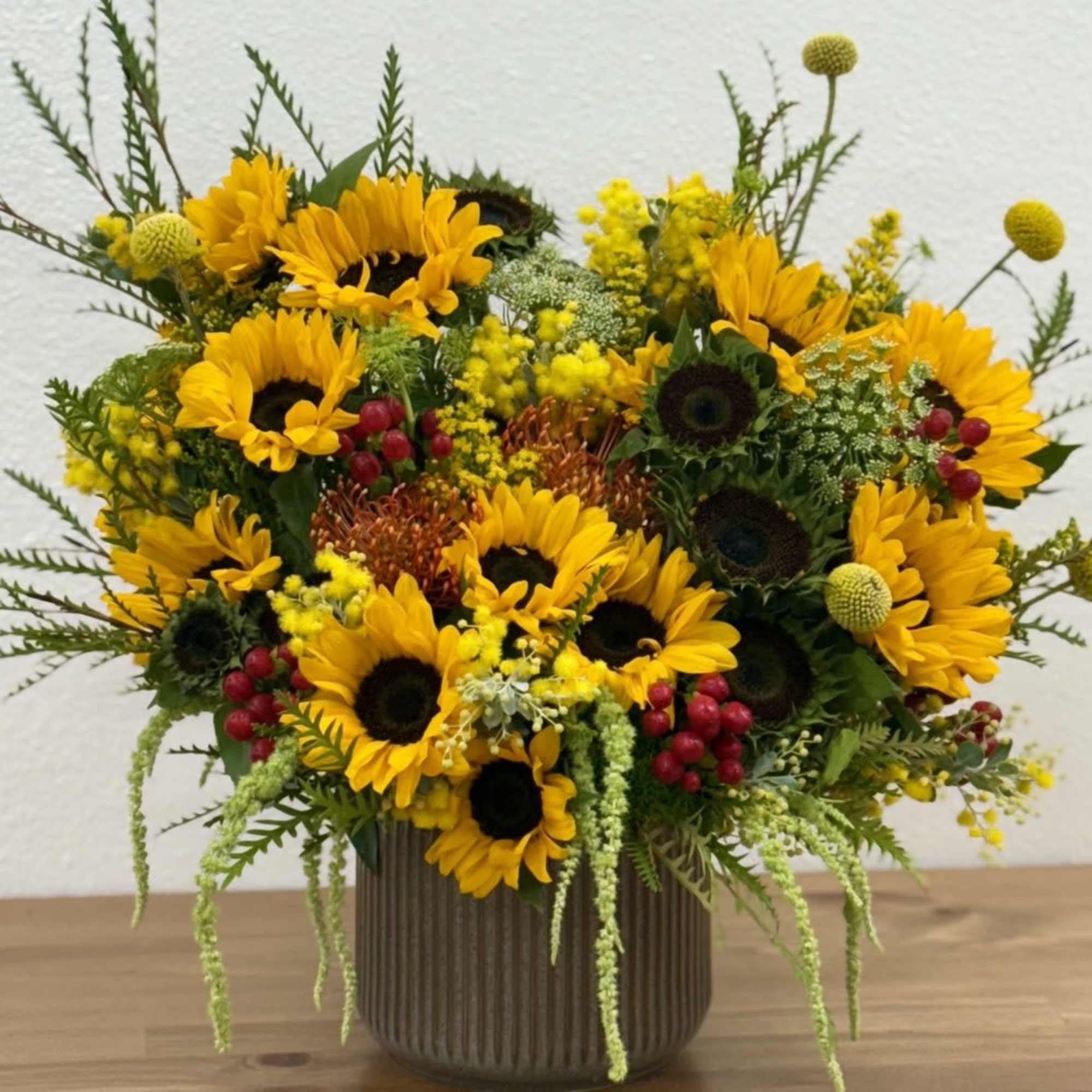 Sunflower arrangement in a ribbed vase with red berry accents
