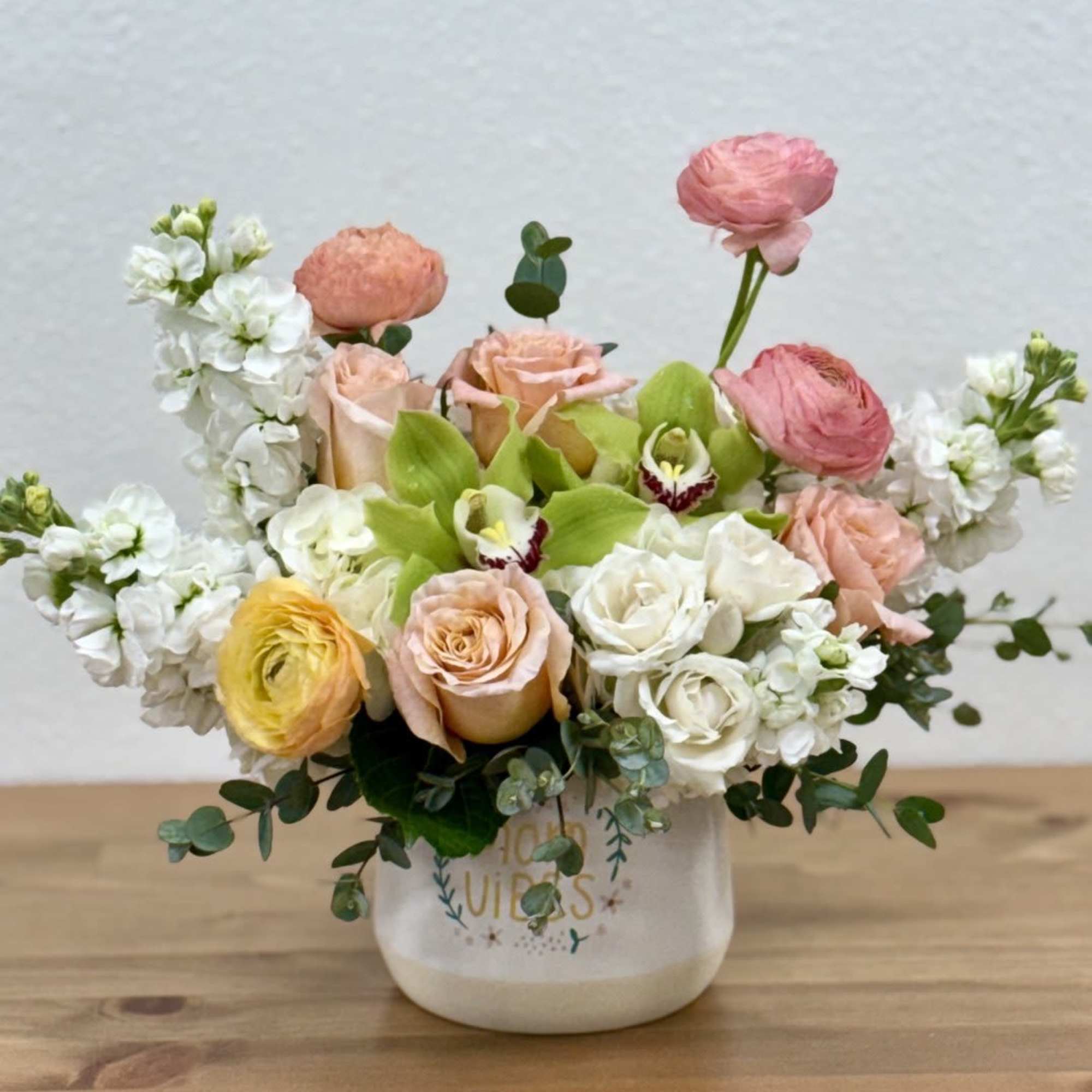 Mixed bouquet of pastel roses, ranunculus, and white blooms in a ceramic vase