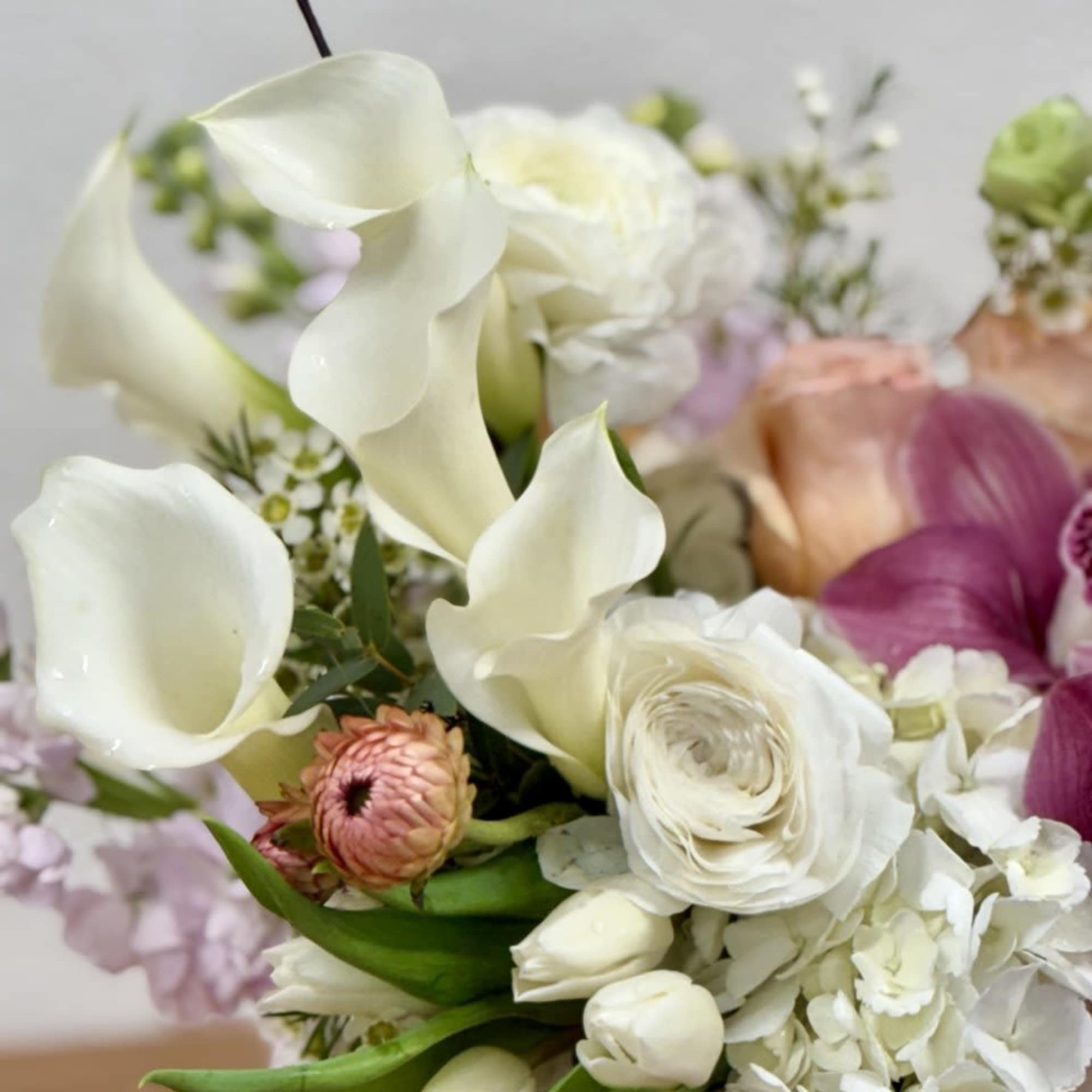 Bouquet of white calla lilies, white ranunculus, and pale hydrangea with pink accents