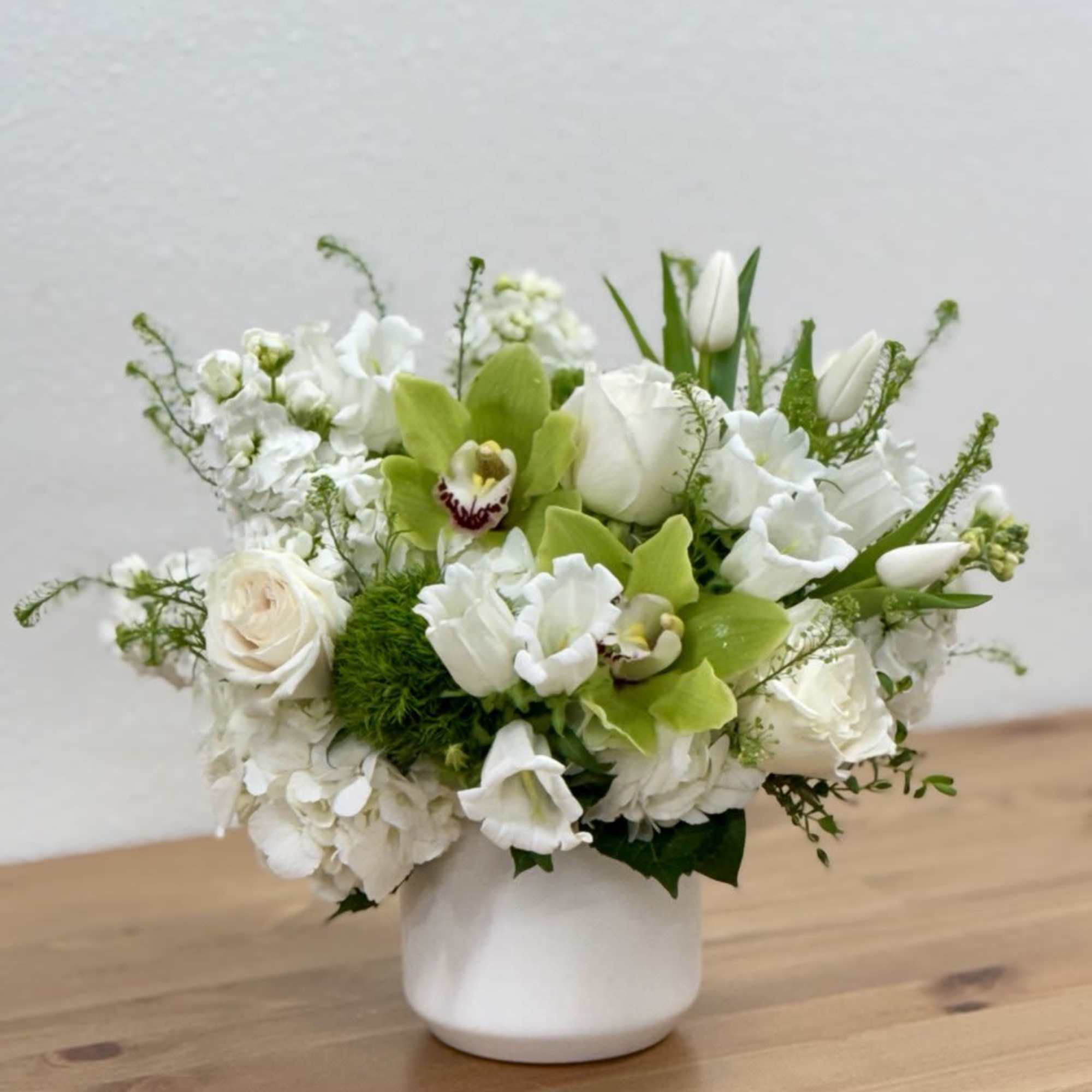 White floral arrangement in a white vase with green orchids and tulips