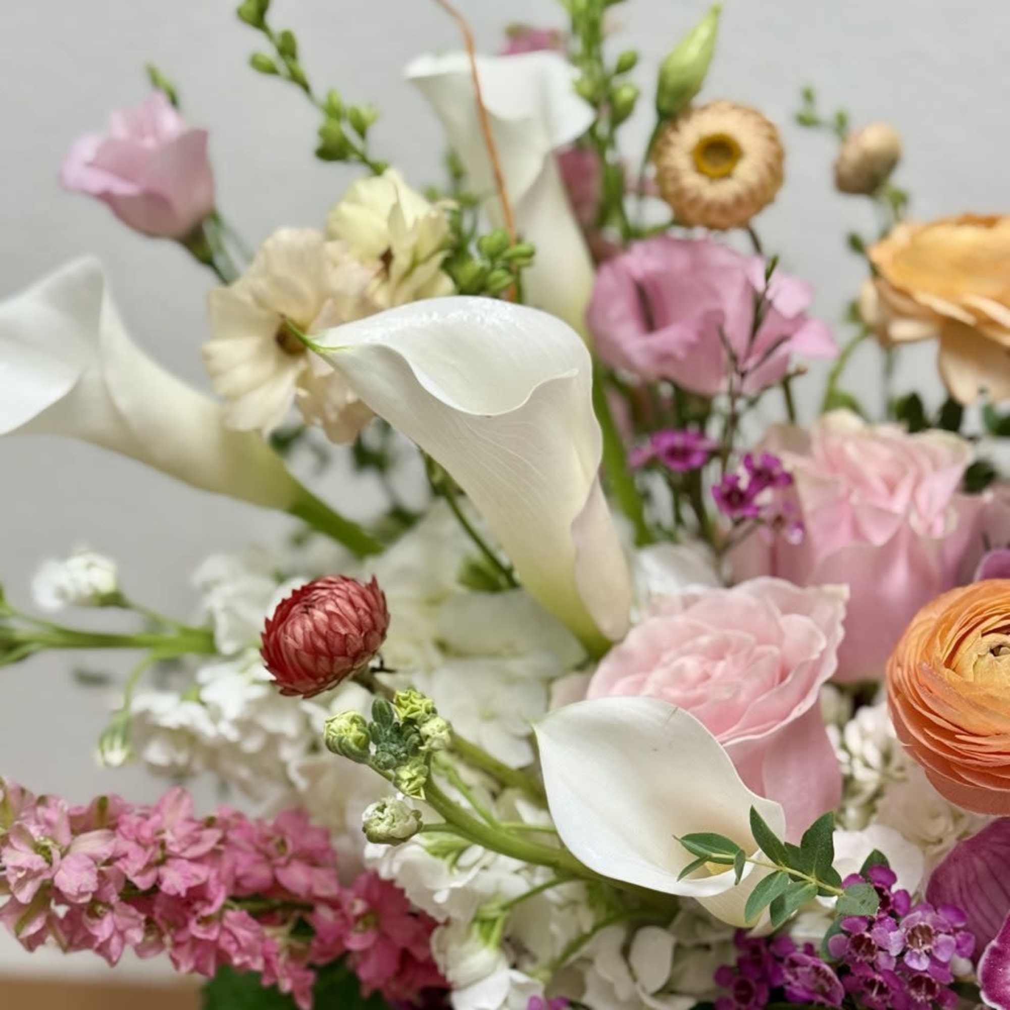 Mixed arrangement of white calla lilies, pink roses, and assorted pastel flowers in a glass vase