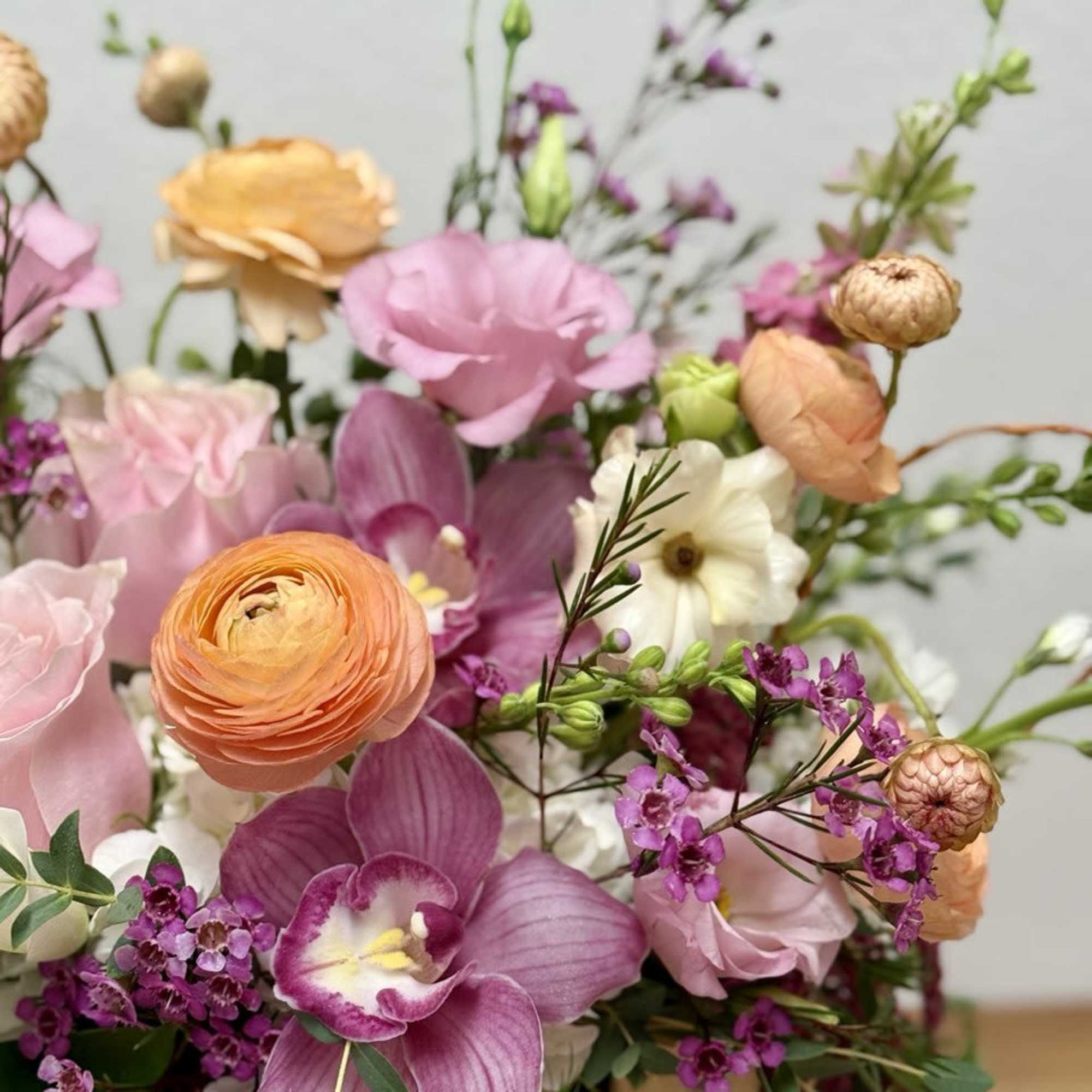 Colorful arrangement of pink orchids, roses, and peach ranunculus in a loose garden-style design
