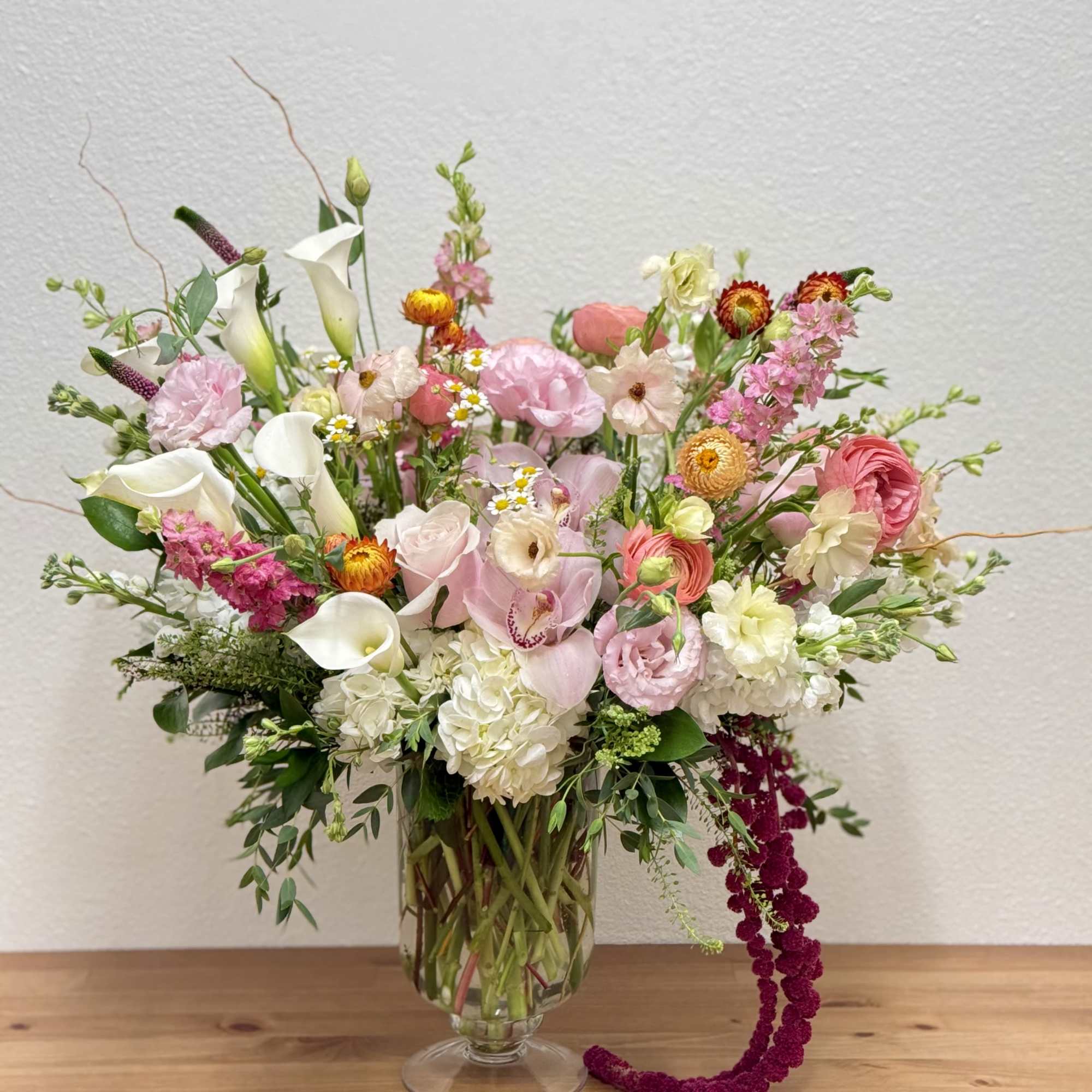 Tall pink and white mixed flower arrangement in a clear glass vase with trailing burgundy accents
