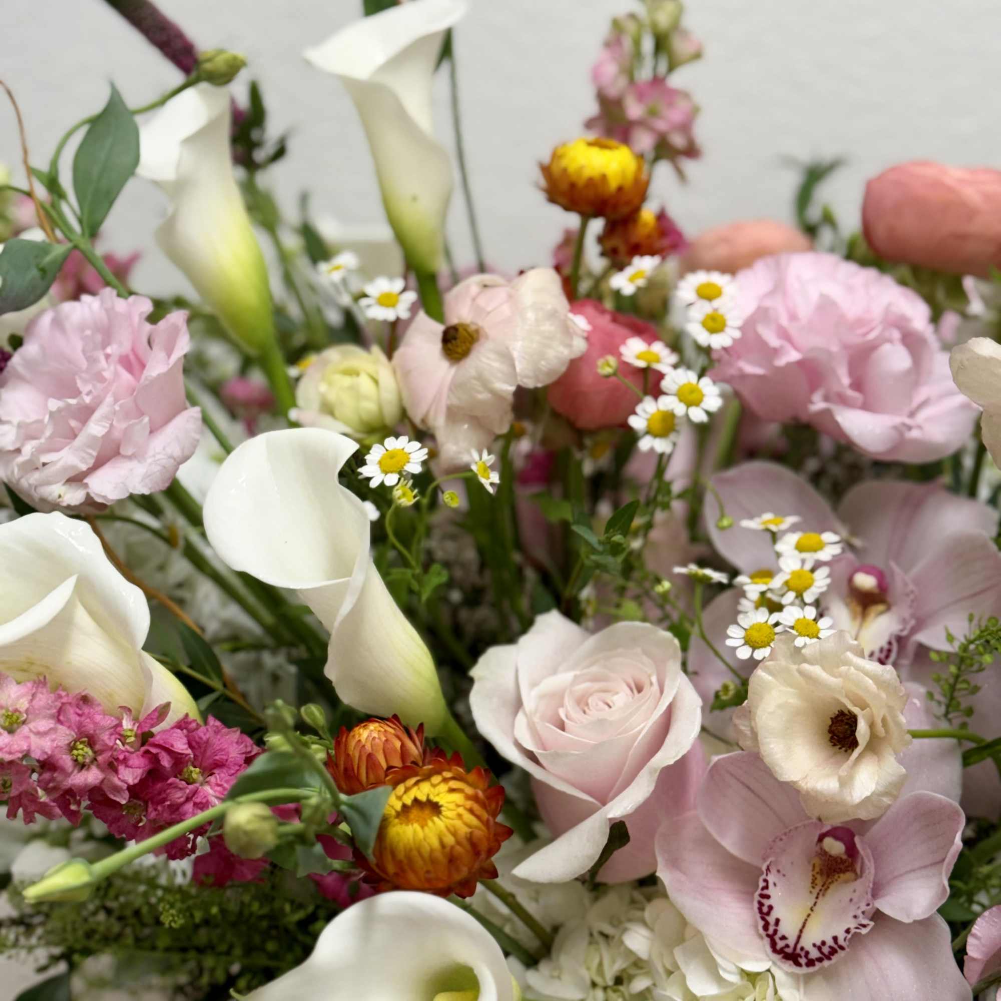Mixed arrangement of pink roses, orchids, ranunculus and white calla lilies with yellow accents
