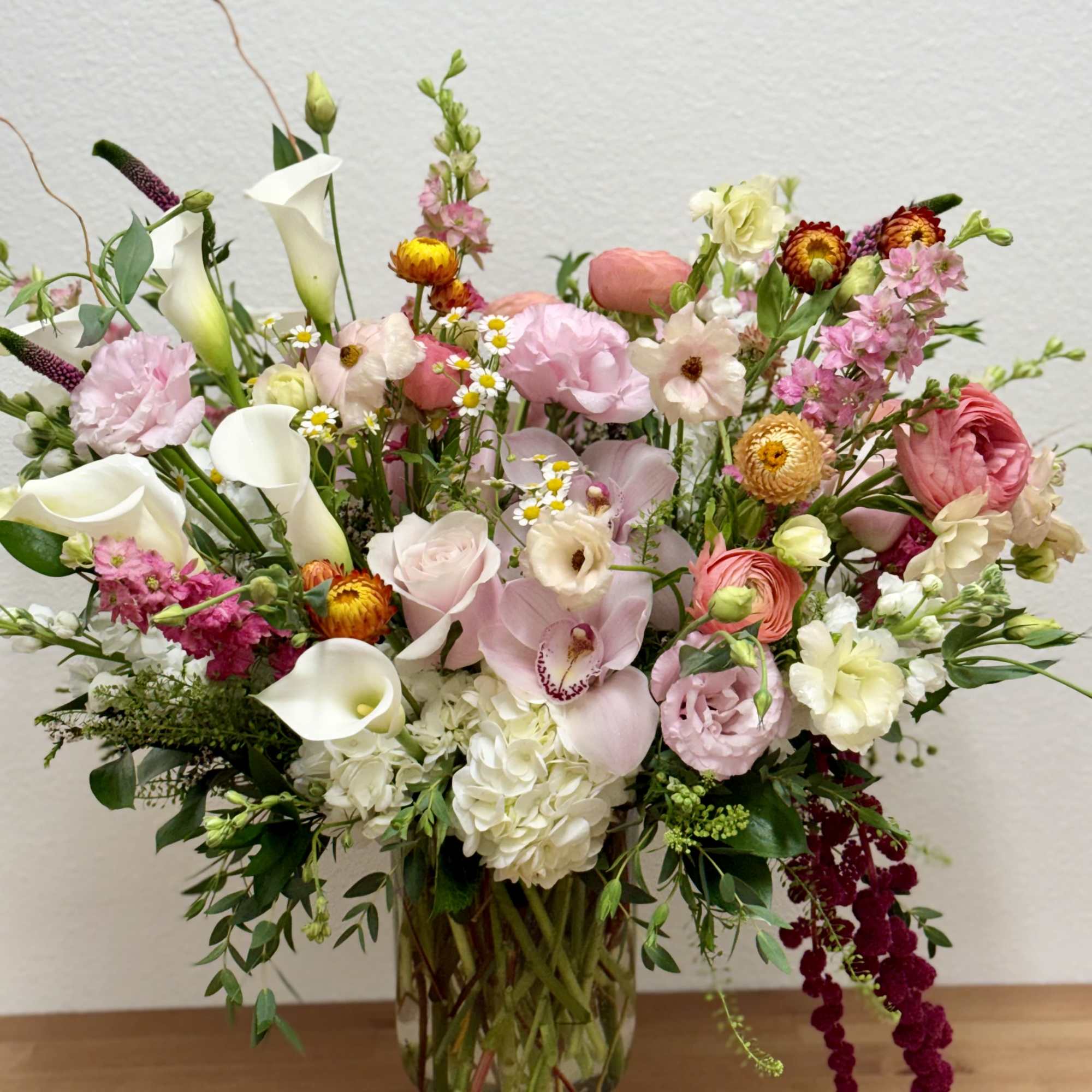Tall mixed arrangement of pink, white, and peach flowers in a clear glass vase on a wooden surface