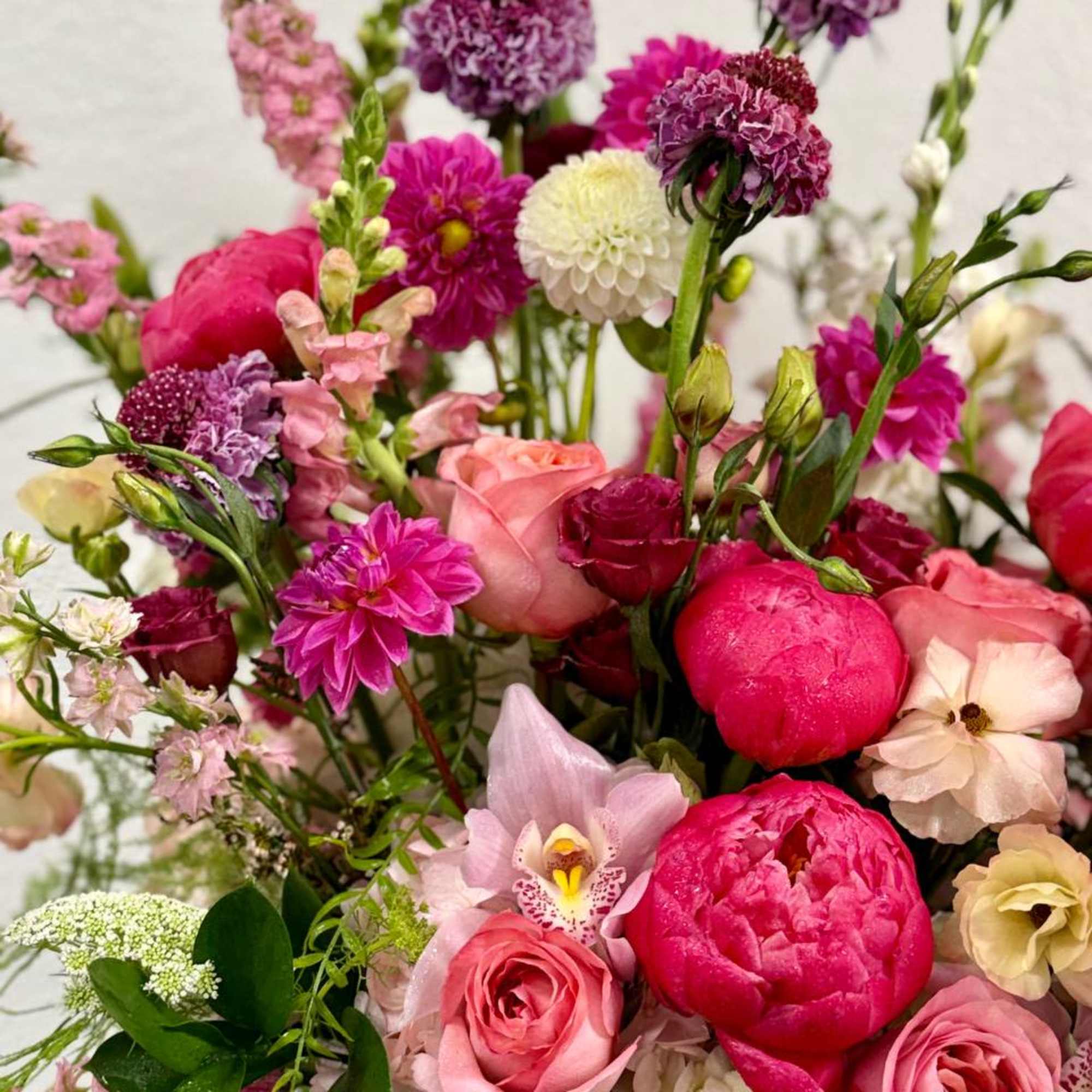 Lush arrangement of pink peonies, roses, dahlias, and white blooms in a garden-style design.
