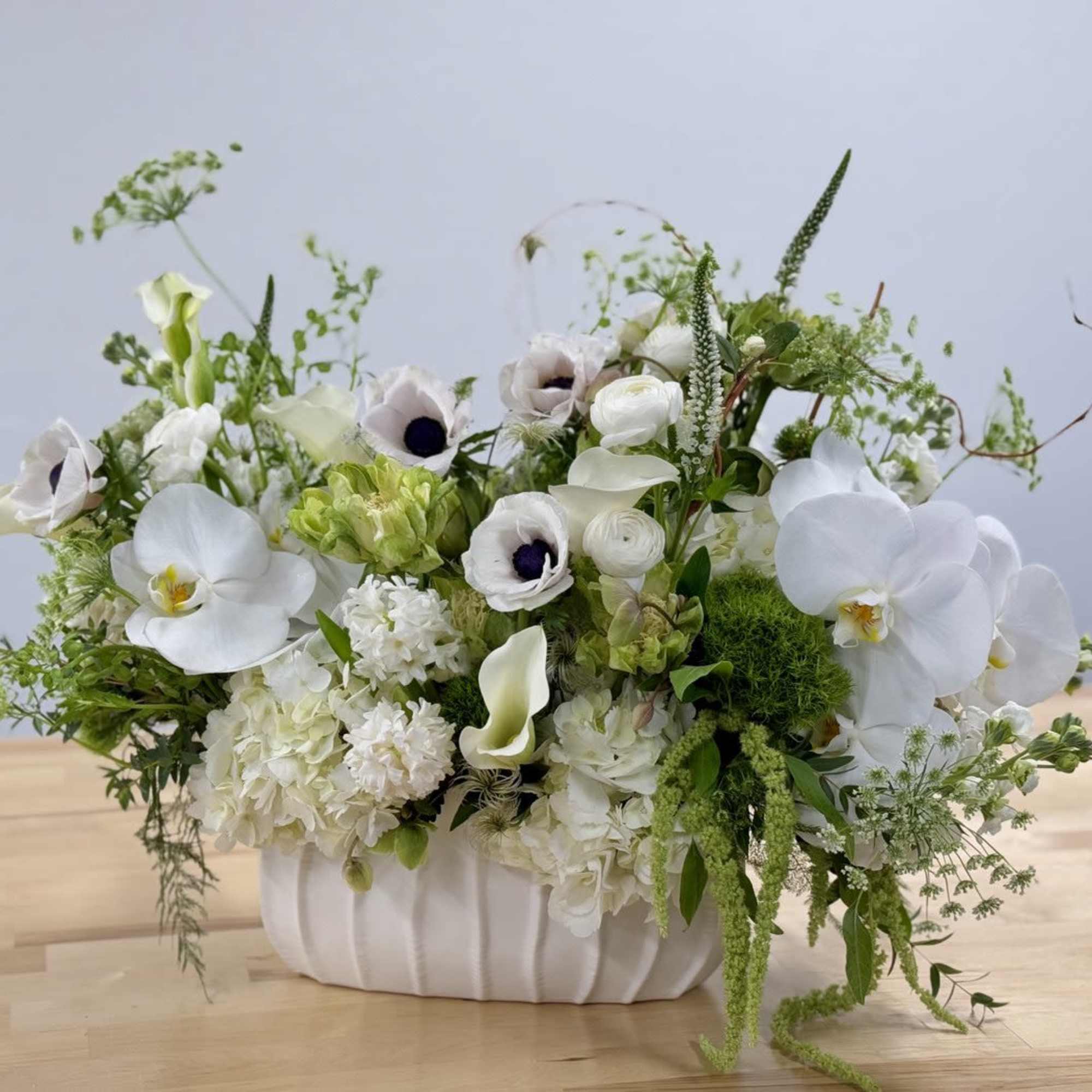 Low white arrangement with orchids, anemones, calla lilies, and hydrangeas in a white ceramic vase