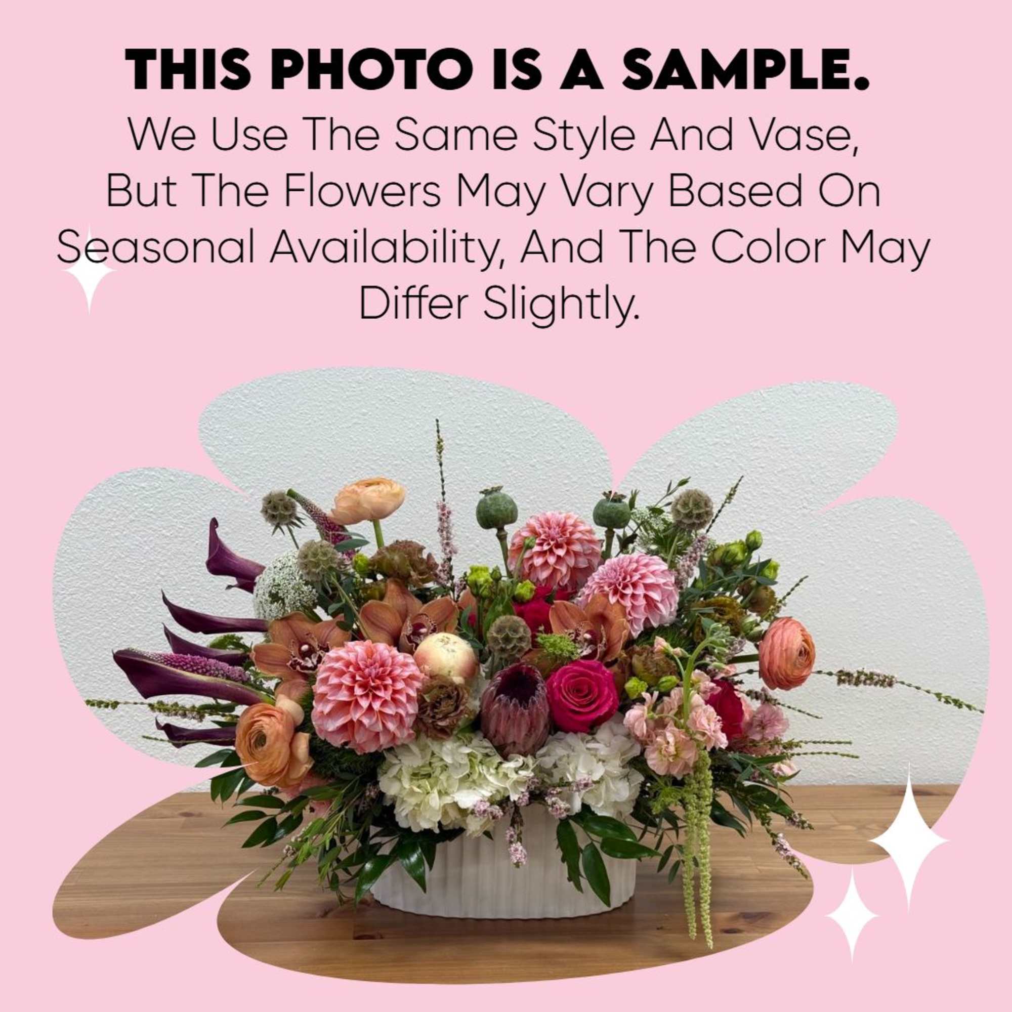 Low centerpiece of pink dahlias, roses, calla lilies, and mixed blooms in a white ceramic vase