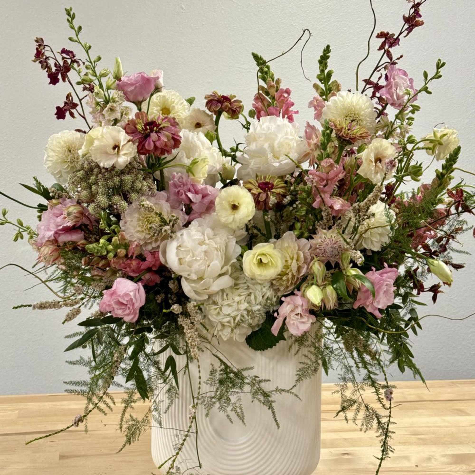 Large airy arrangement of white and pink flowers with burgundy accents in a tall white ceramic vase.