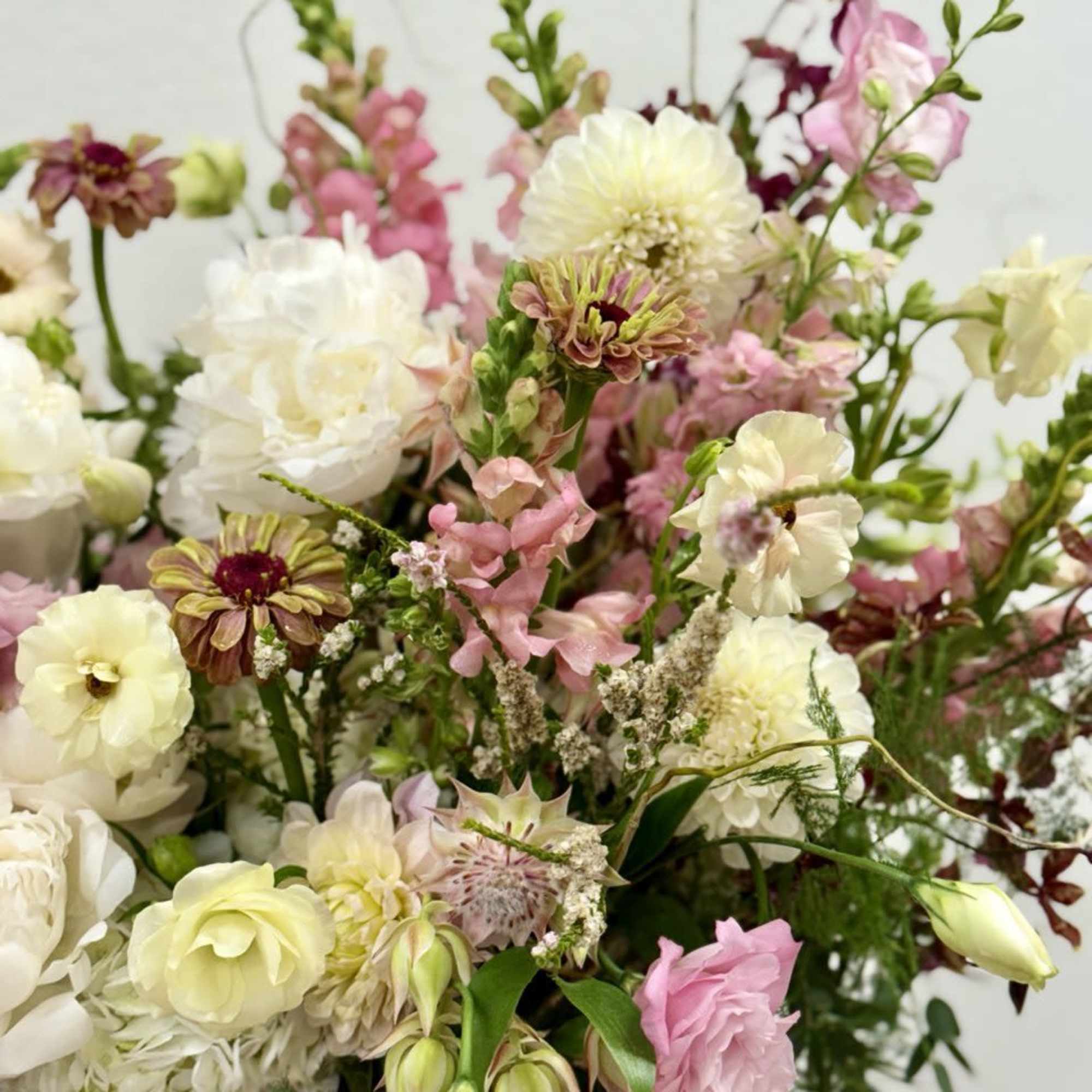 Loose garden-style arrangement of pink and ivory flowers with tall snapdragons and dahlias.