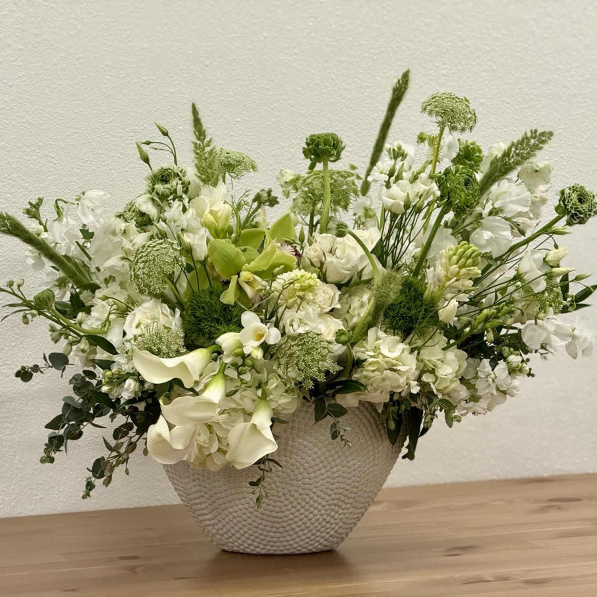 White and green flower arrangement in a textured white bowl on a wooden surface