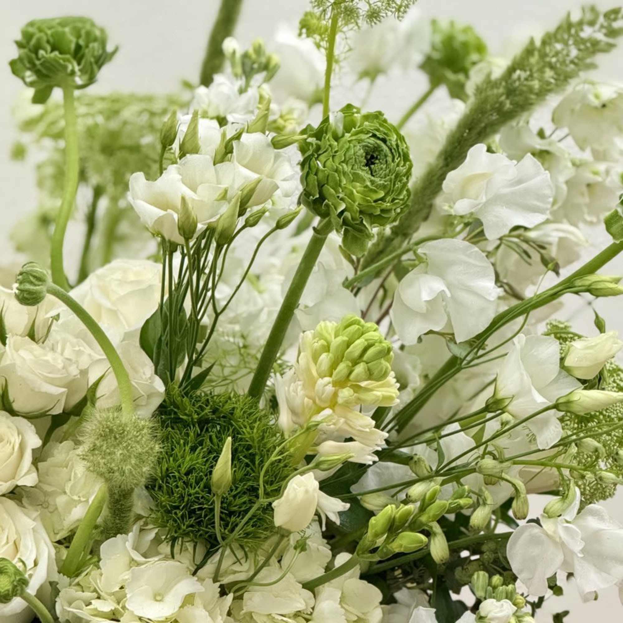 Arrangement of white and green flowers including roses and hydrangeas in a loose, airy design.