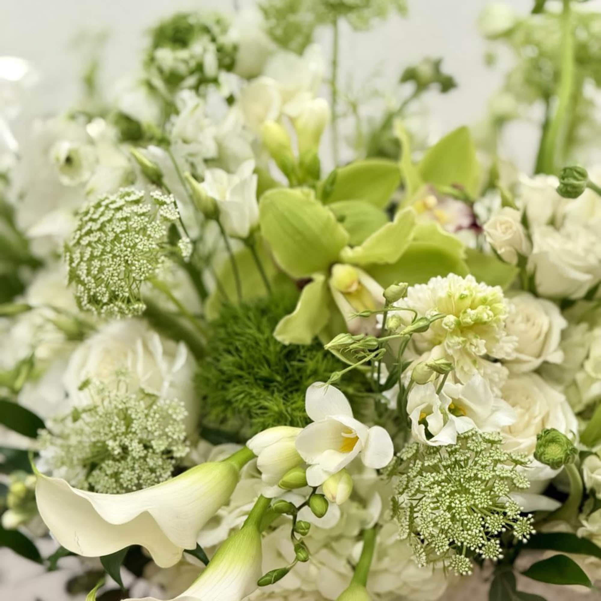White and green floral arrangement with calla lilies, roses, orchids, and hydrangeas in an airy design