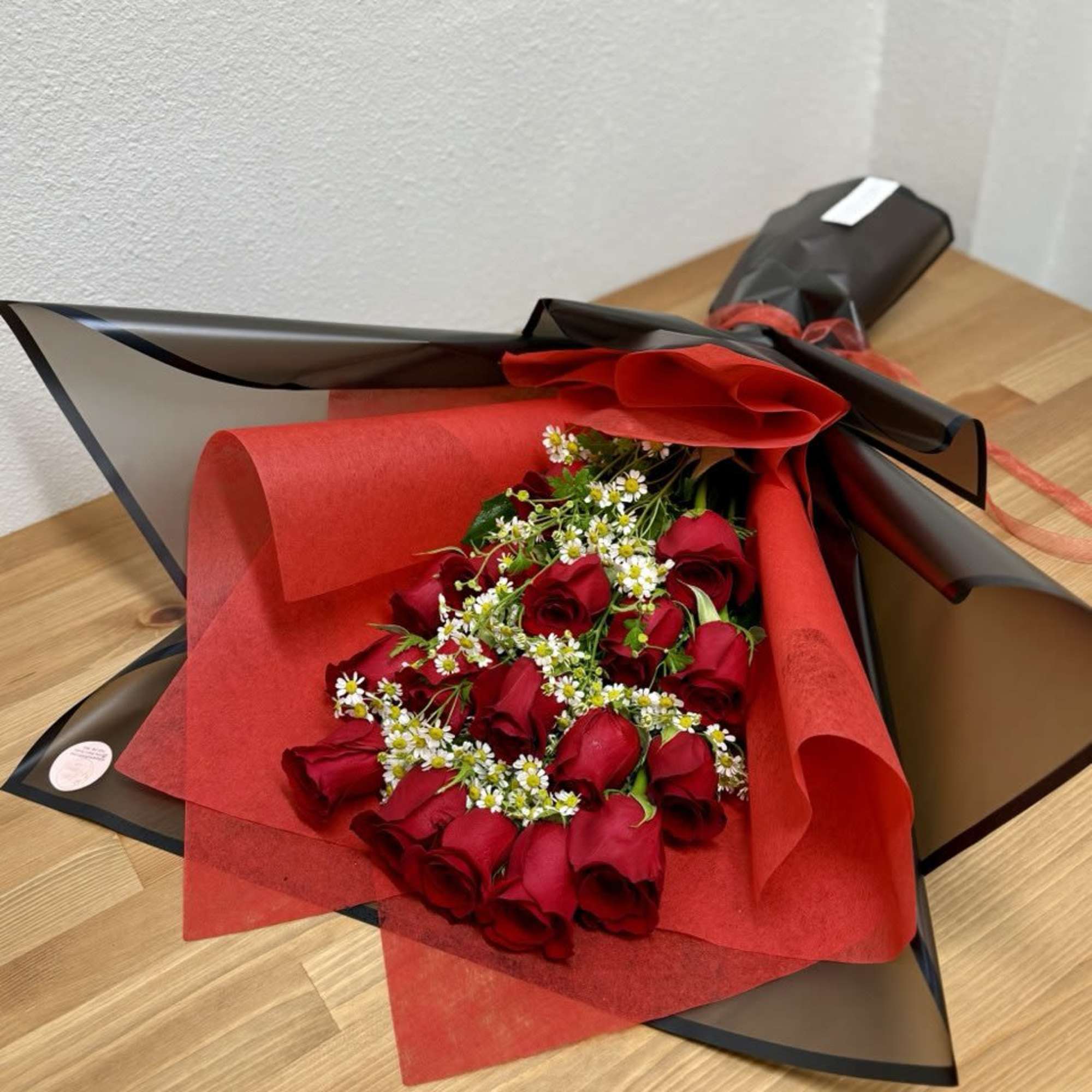 Bouquet of red roses with small white filler flowers in black and red wrap