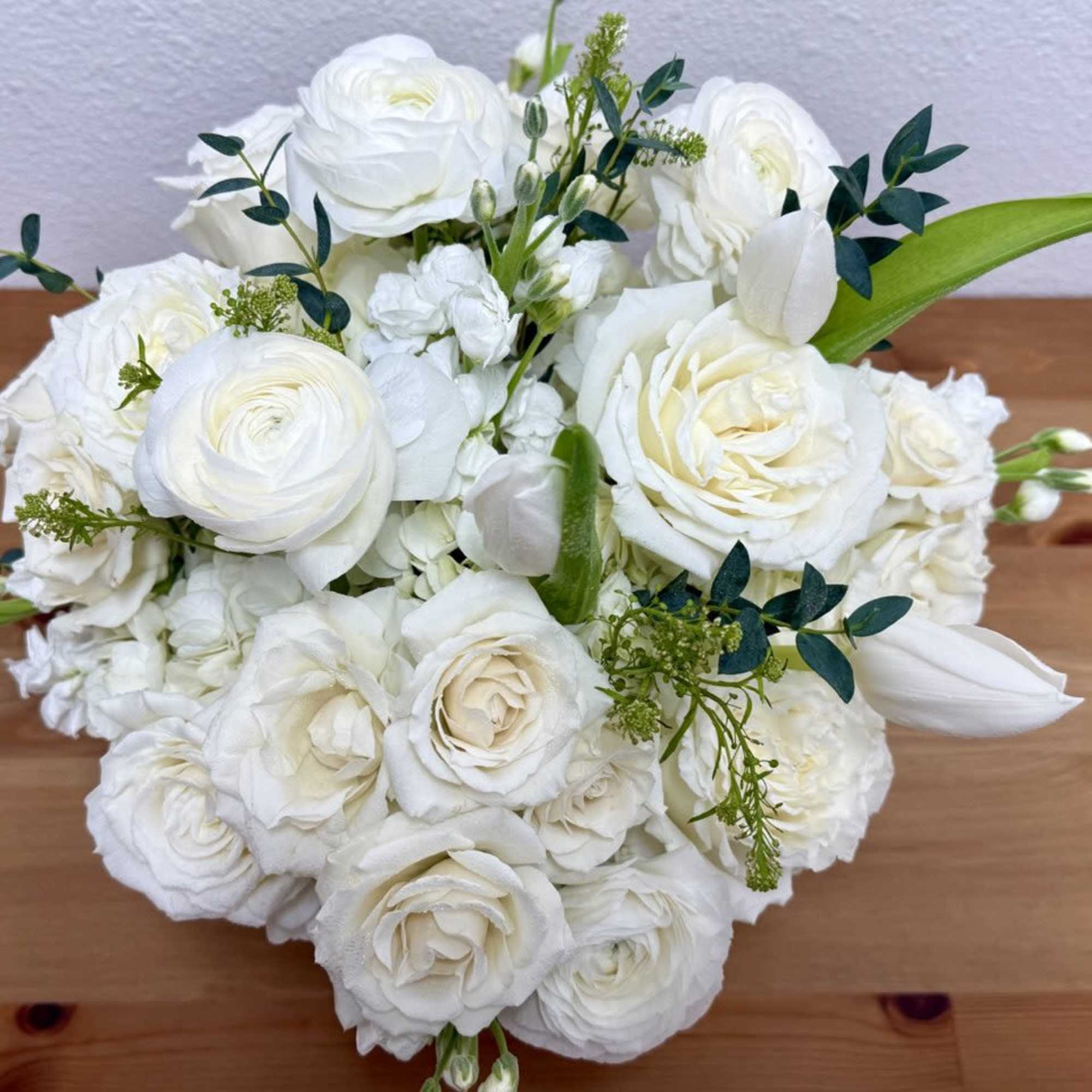 White rose bouquet with small green accents on a wooden table