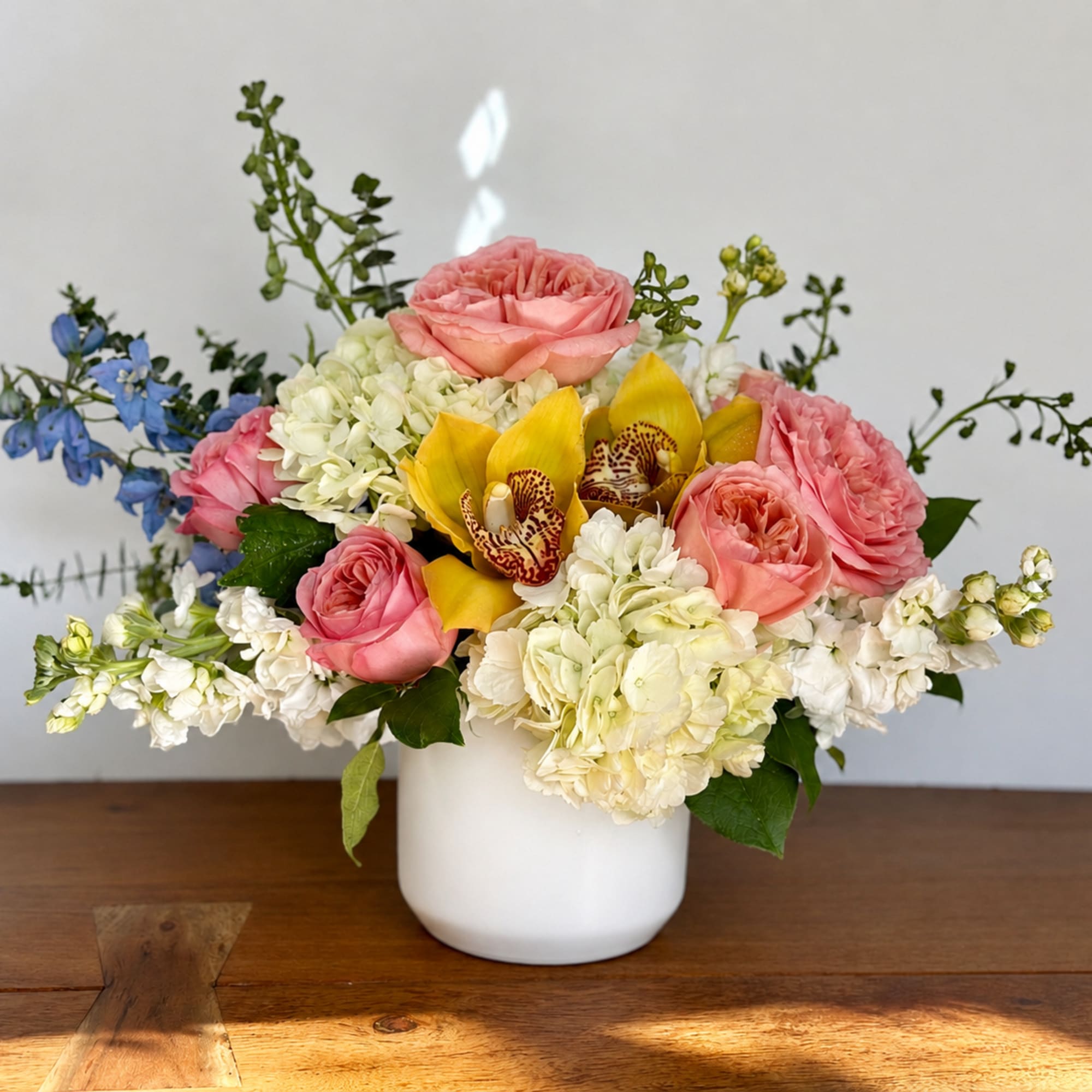 Pink roses, white hydrangeas, and yellow orchids in a white vase