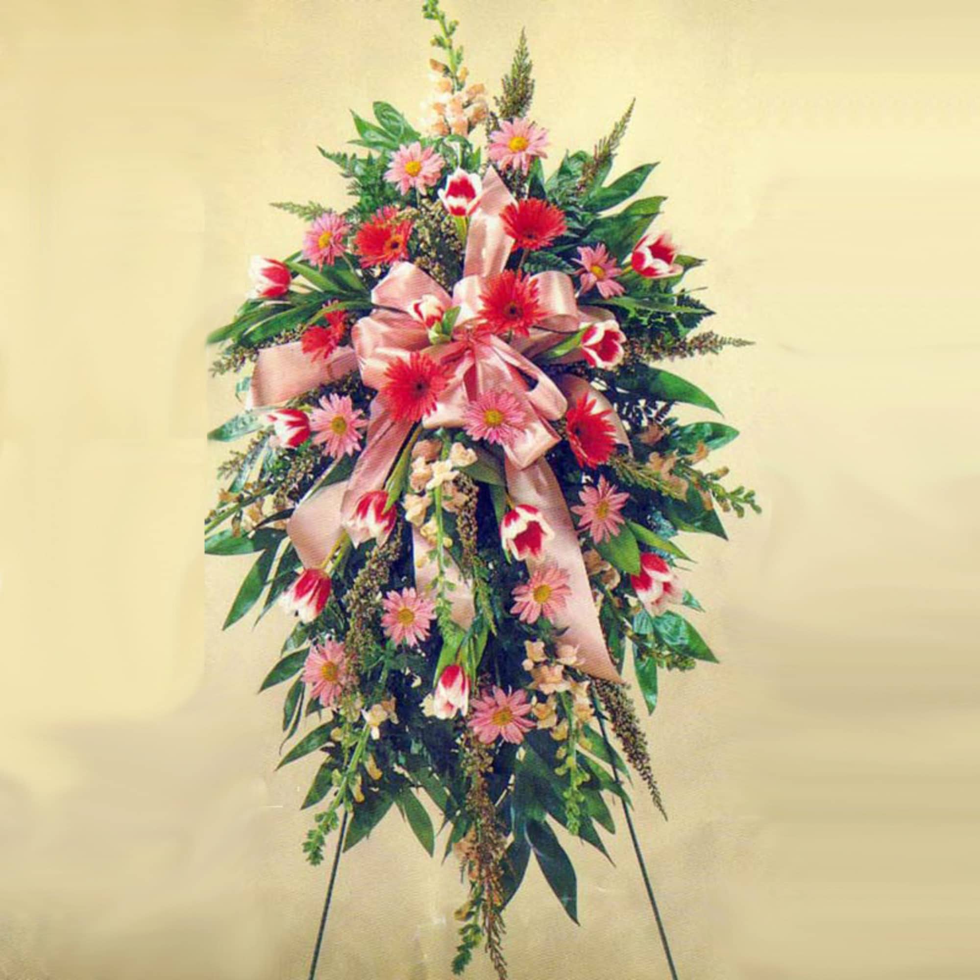 Standing spray with pink and red flowers, tulips, and a large pink ribbon on an easel