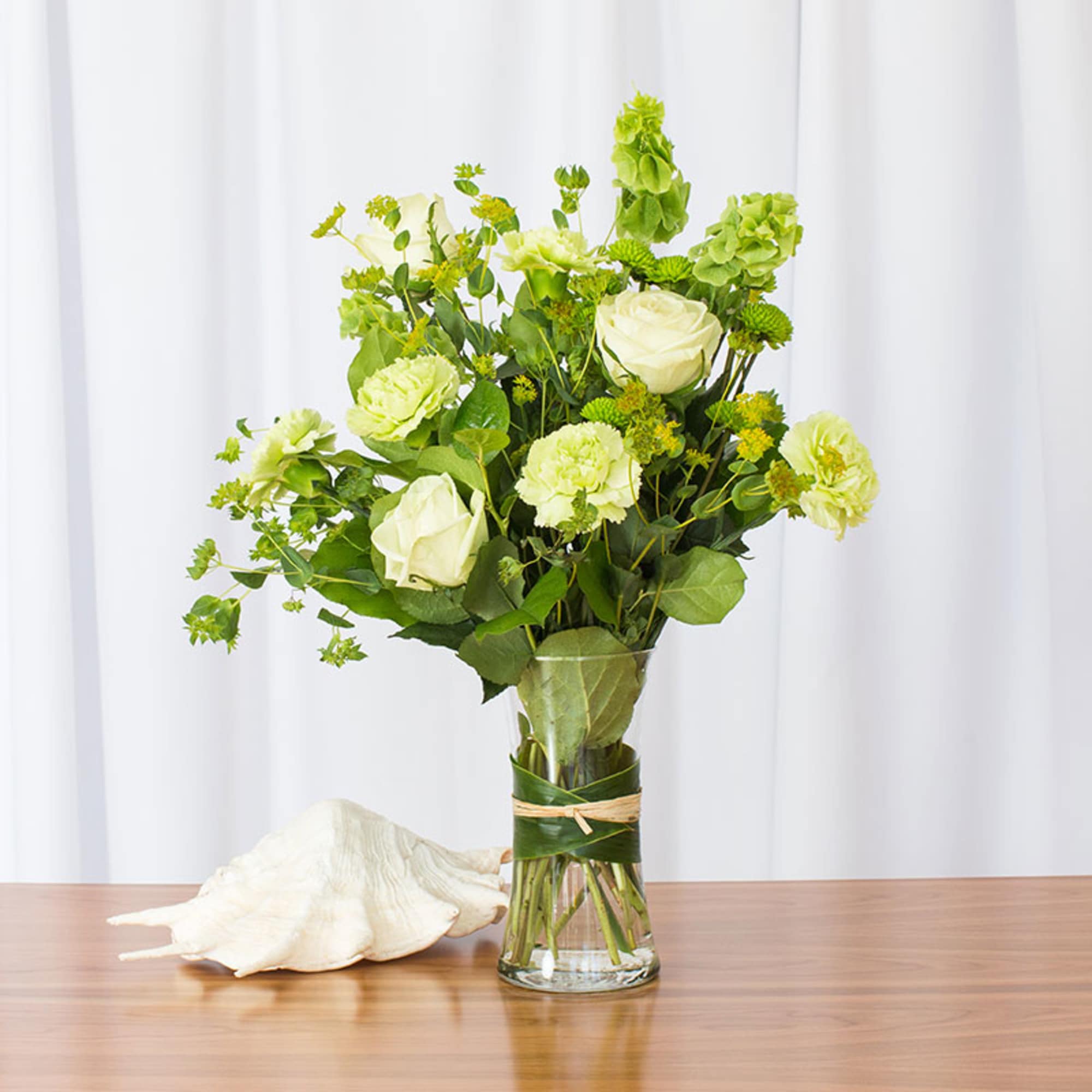 Green and white bouquet with roses and carnations in a clear glass vase on a table