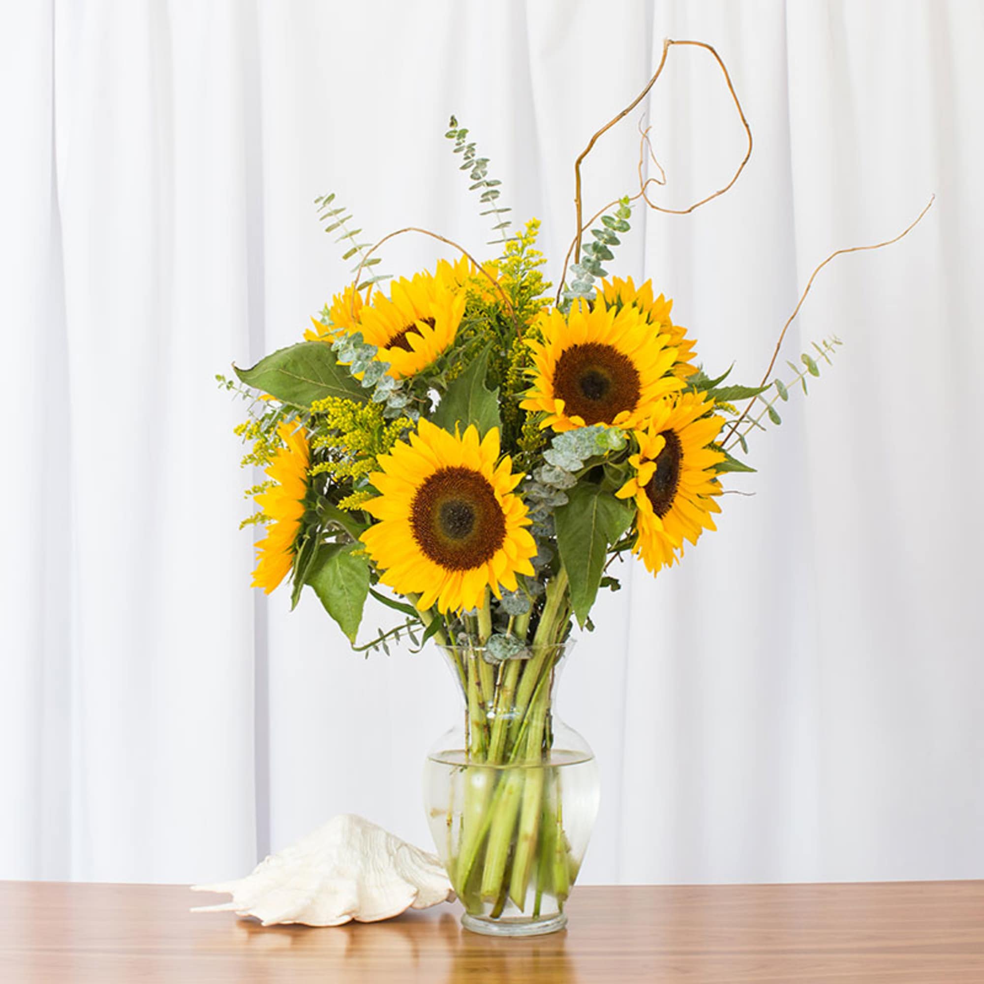 Bouquet of bright yellow sunflowers in a clear glass vase on a wooden table.