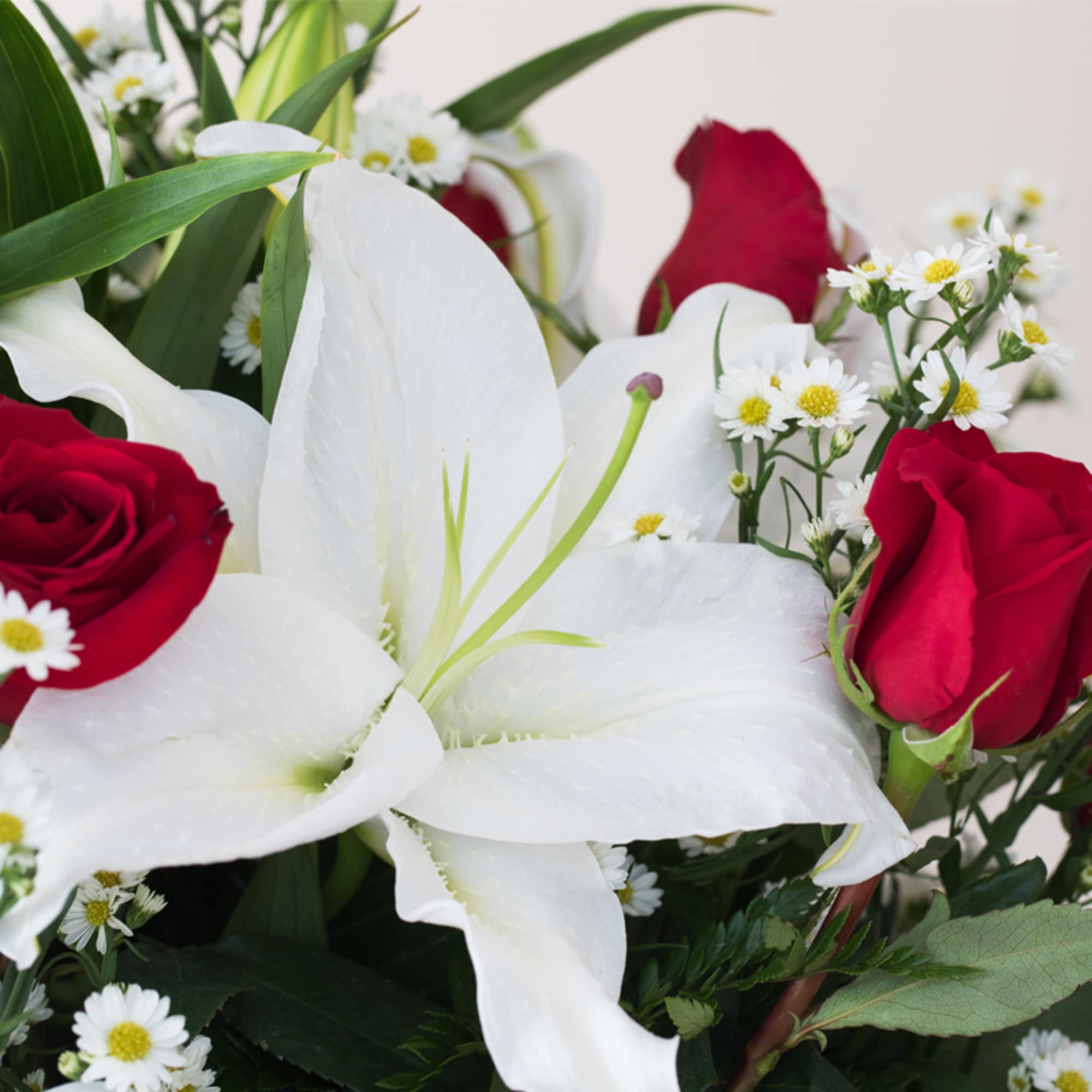 Arrangement of large white lilies with red roses and small white daisies