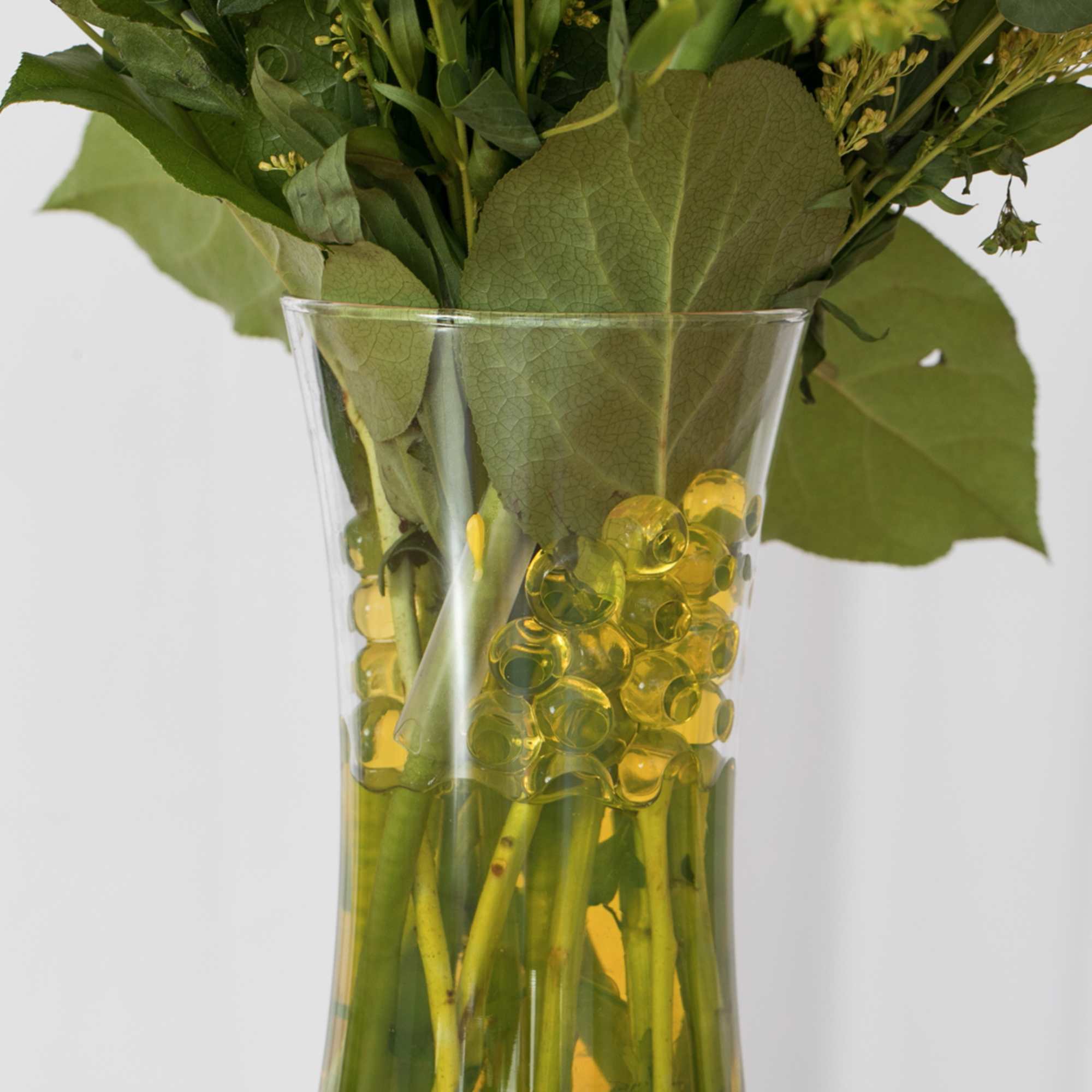 Clear glass vase with yellow water beads and green flower stems
