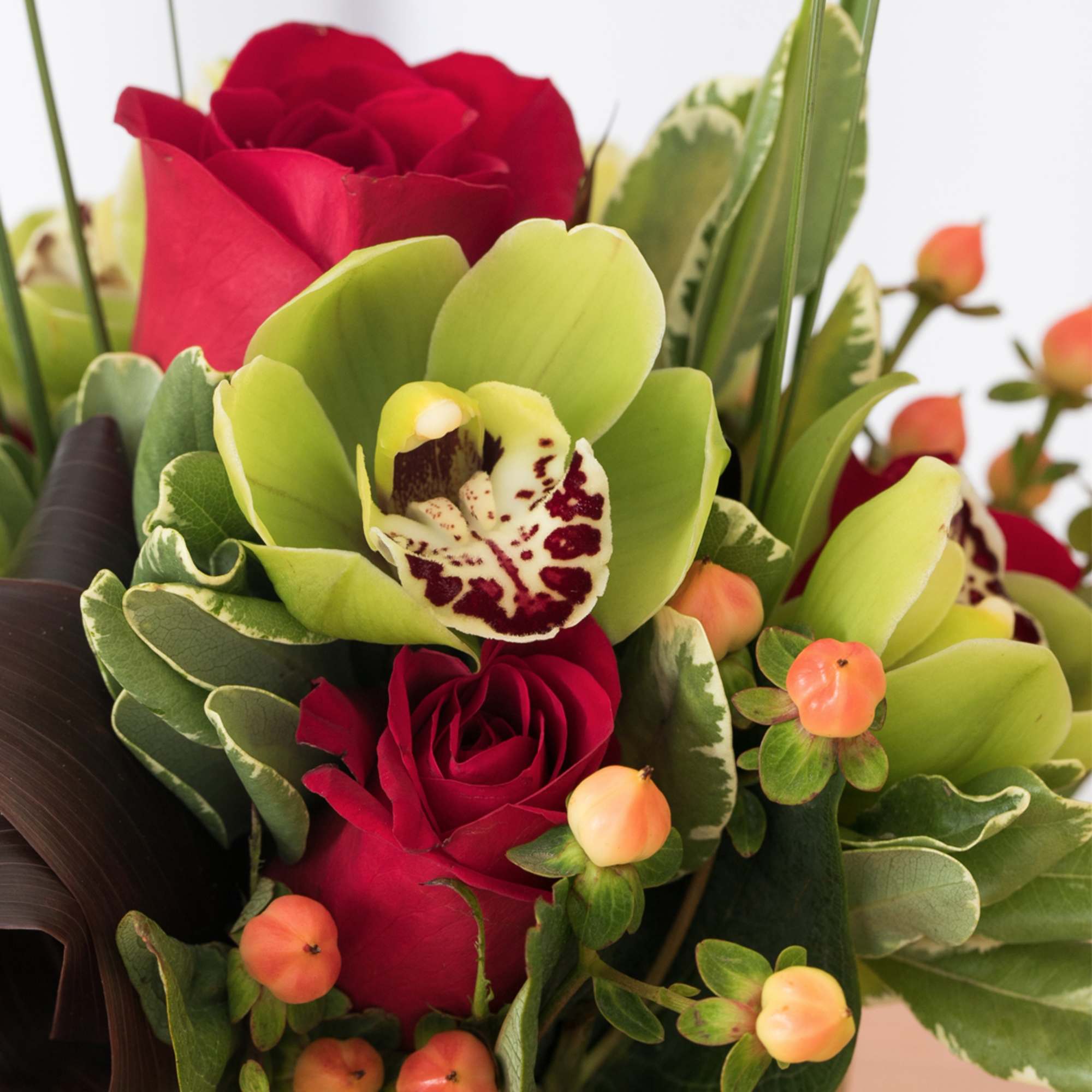 Close-up of red roses, green cymbidium orchids, and peach berries in a compact arrangement.