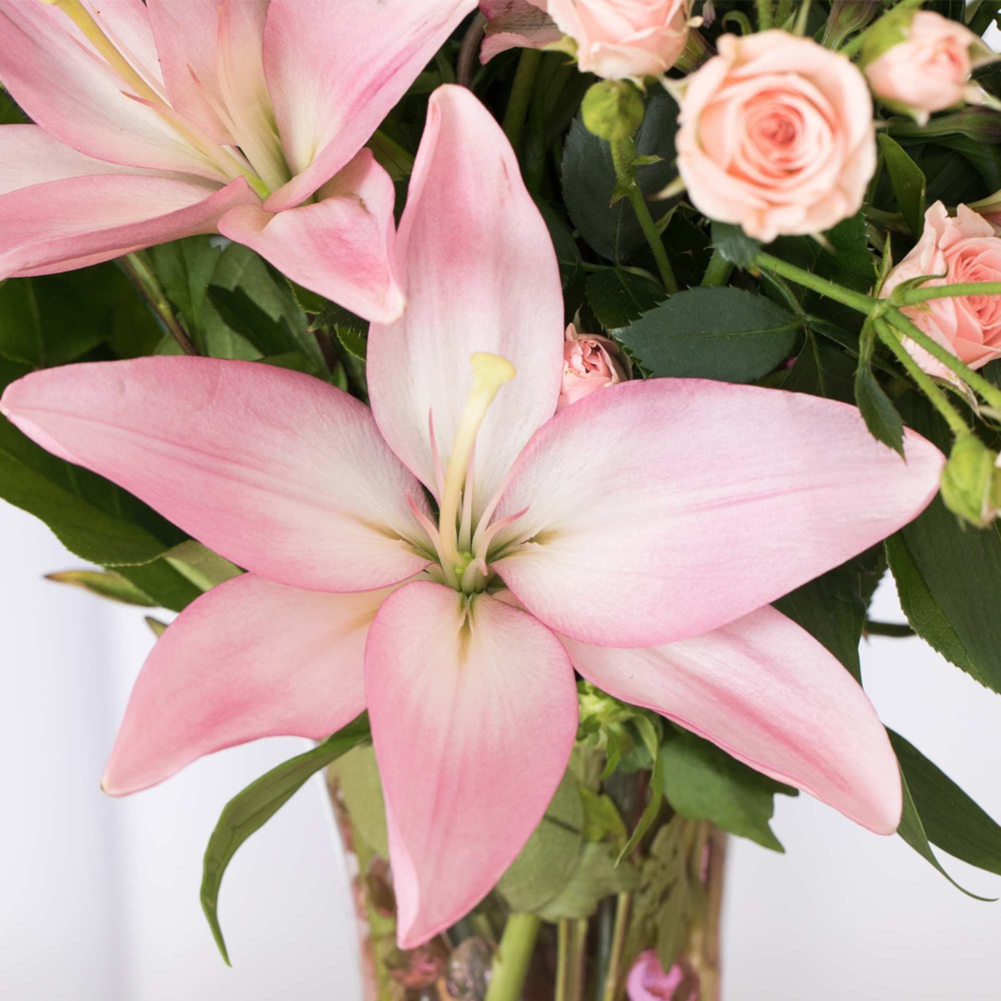 Close-up of pink lilies and pale pink roses in a clear glass vase