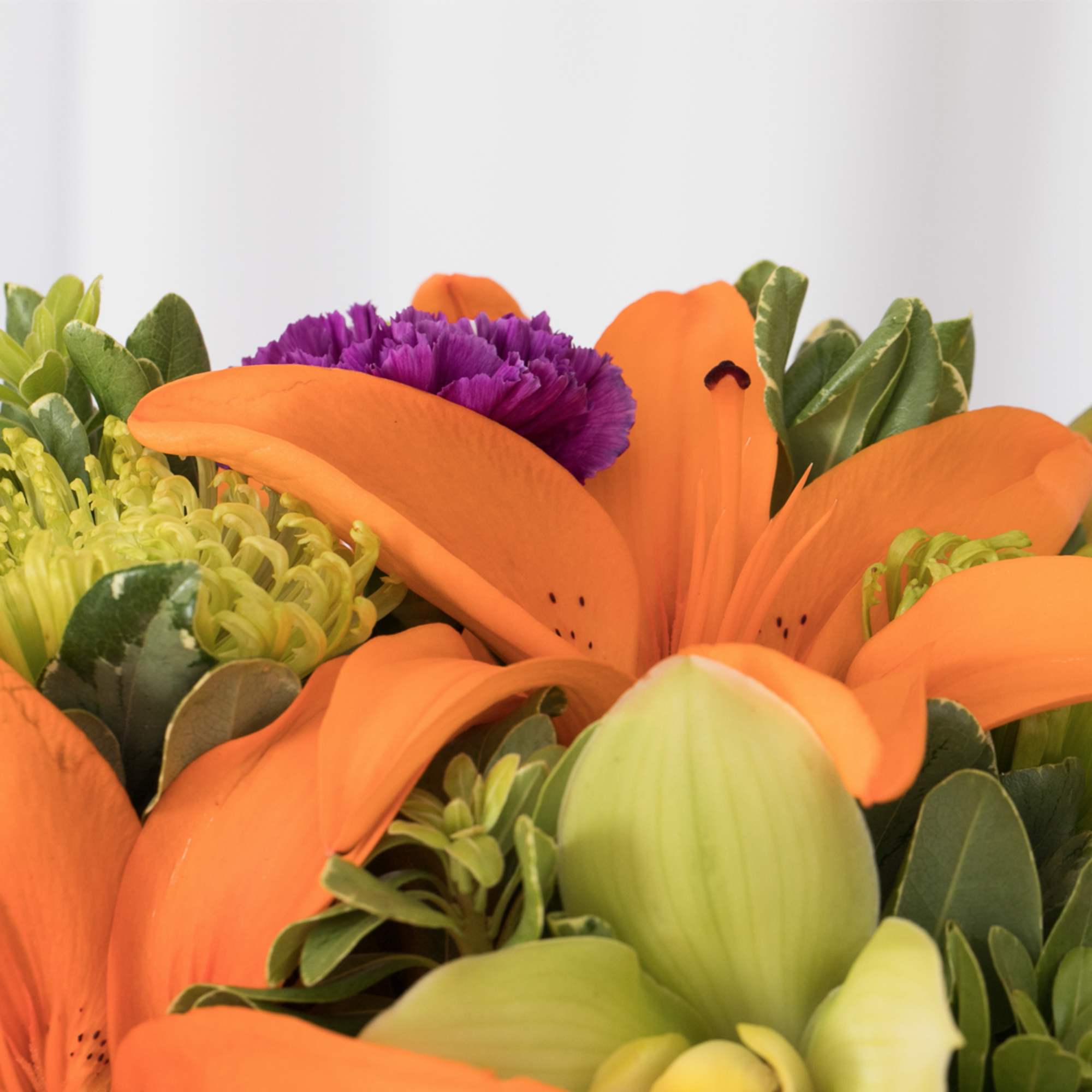 Close-up of an arrangement with bright orange lilies, green blooms, and a purple carnation.