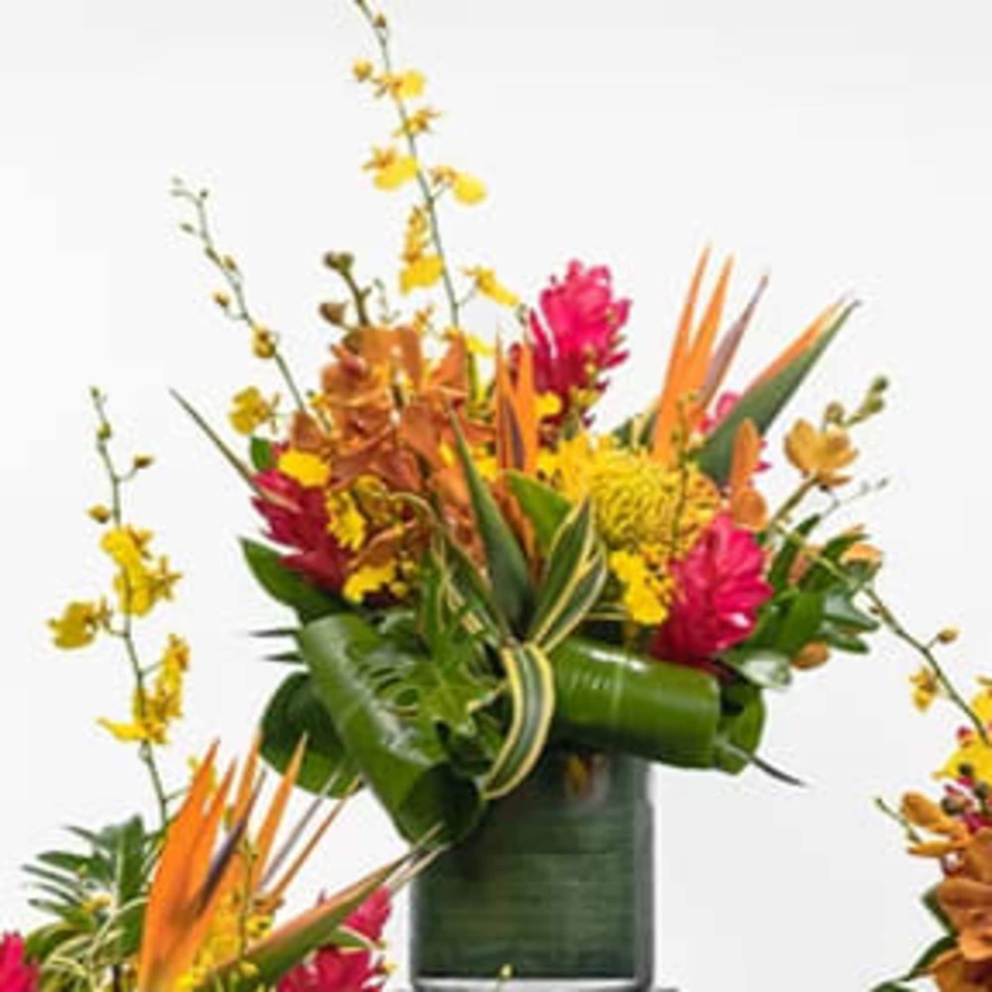Tropical arrangement with orange birds of paradise and pink flowers in a green-wrapped glass vase