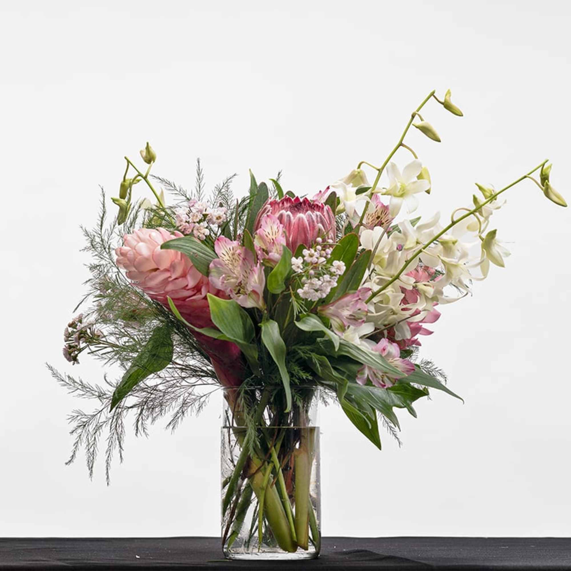 Tall pink and white tropical flower arrangement with orchids and protea in a clear glass vase