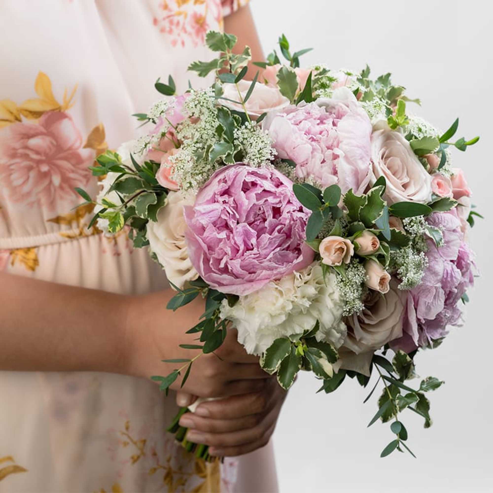 Bridal-style hand-tied bouquet of pink peonies and blush roses held by a person in a floral dress