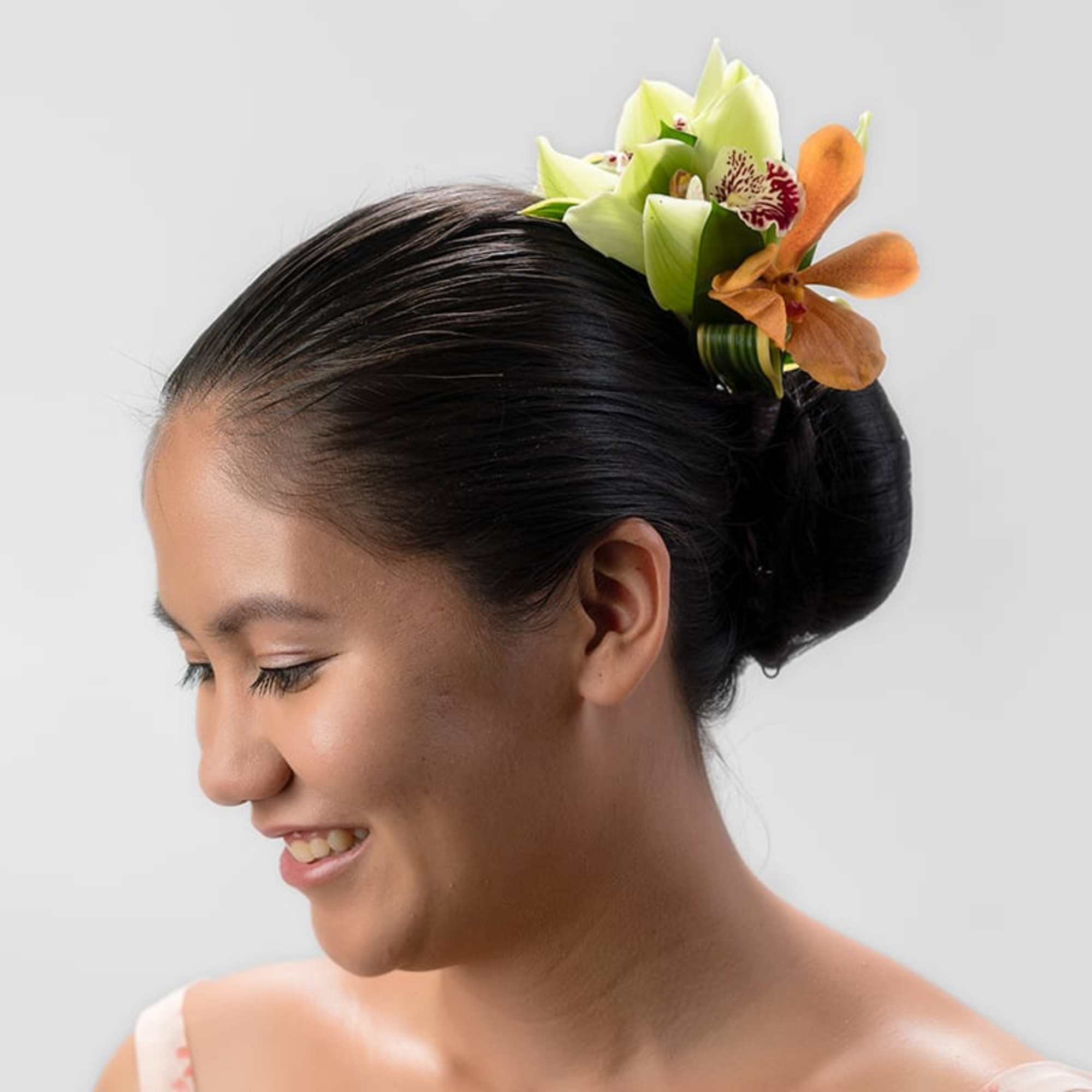 Woman with sleek updo wearing a hairpiece of green and orange orchids above her bun