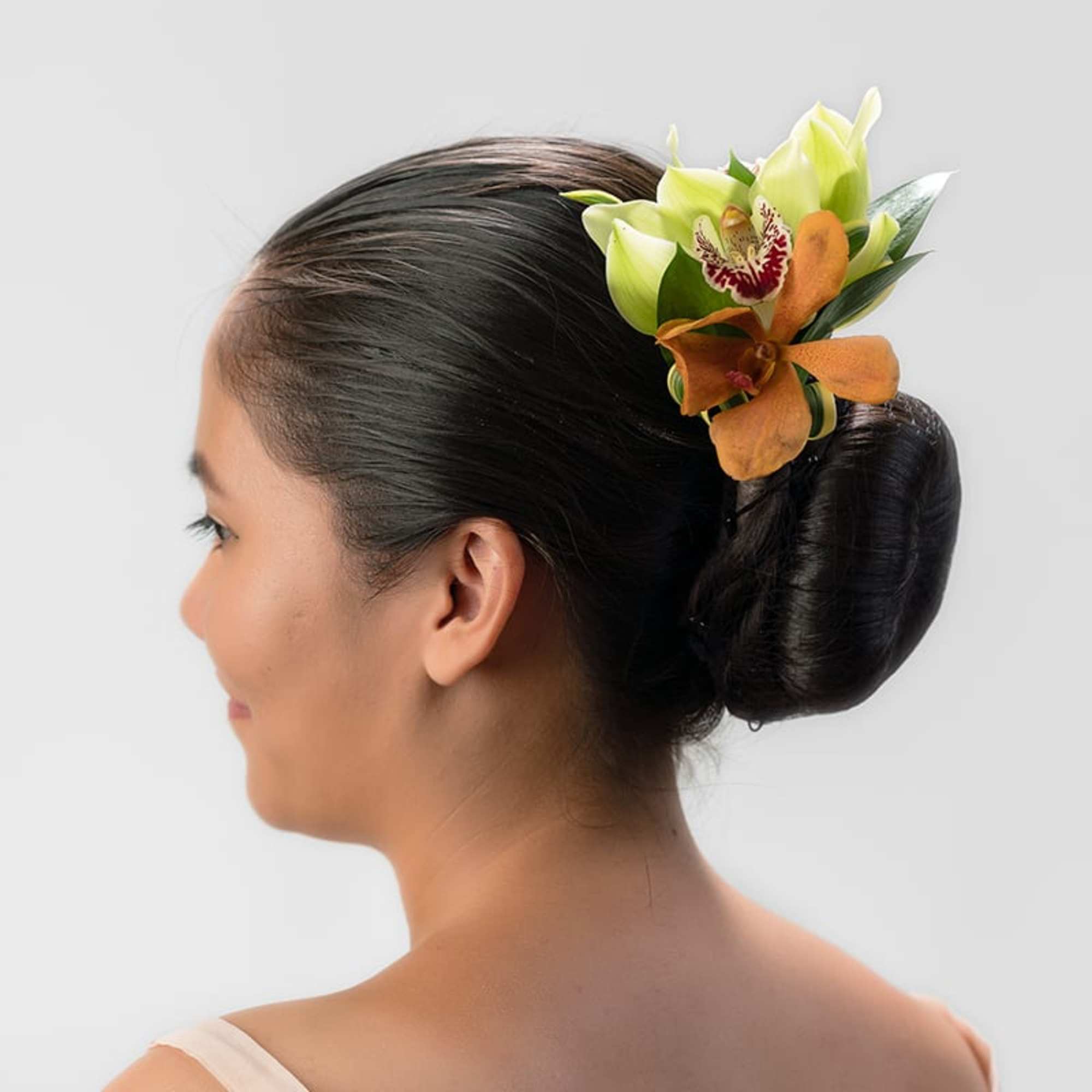 Woman with a sleek bun wearing green and orange orchid hair flowers